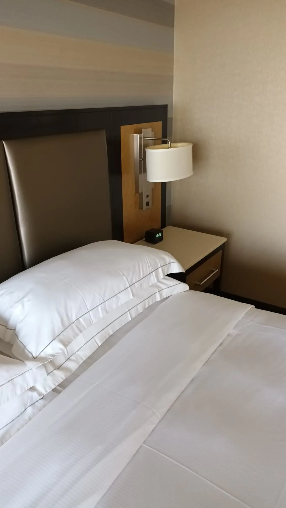 Doppelbett im Hotelzimmer mit grauem Kopfteil und Nachttisch