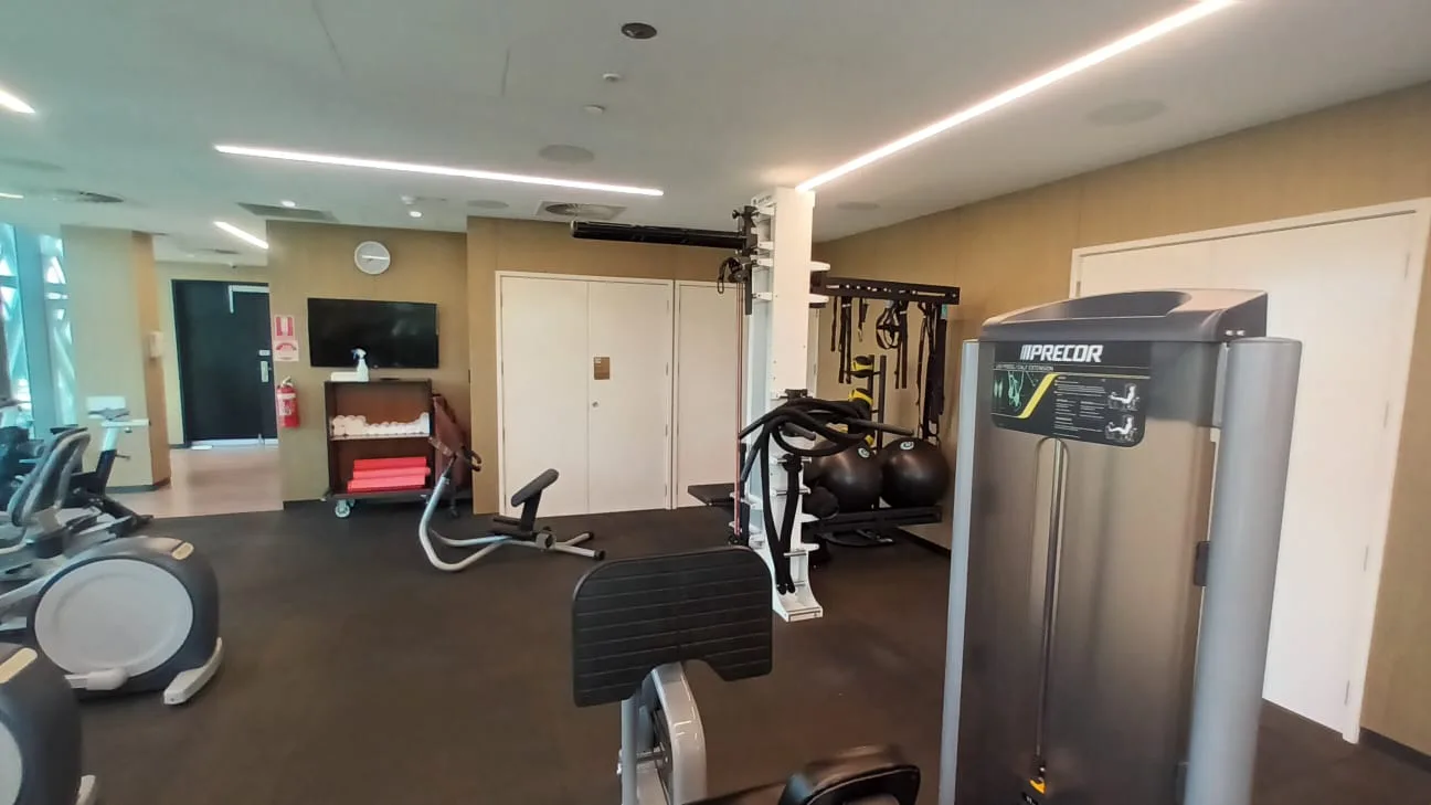 Fitnessraum mit verschiedenen Trainingsgeräten und Wandregal