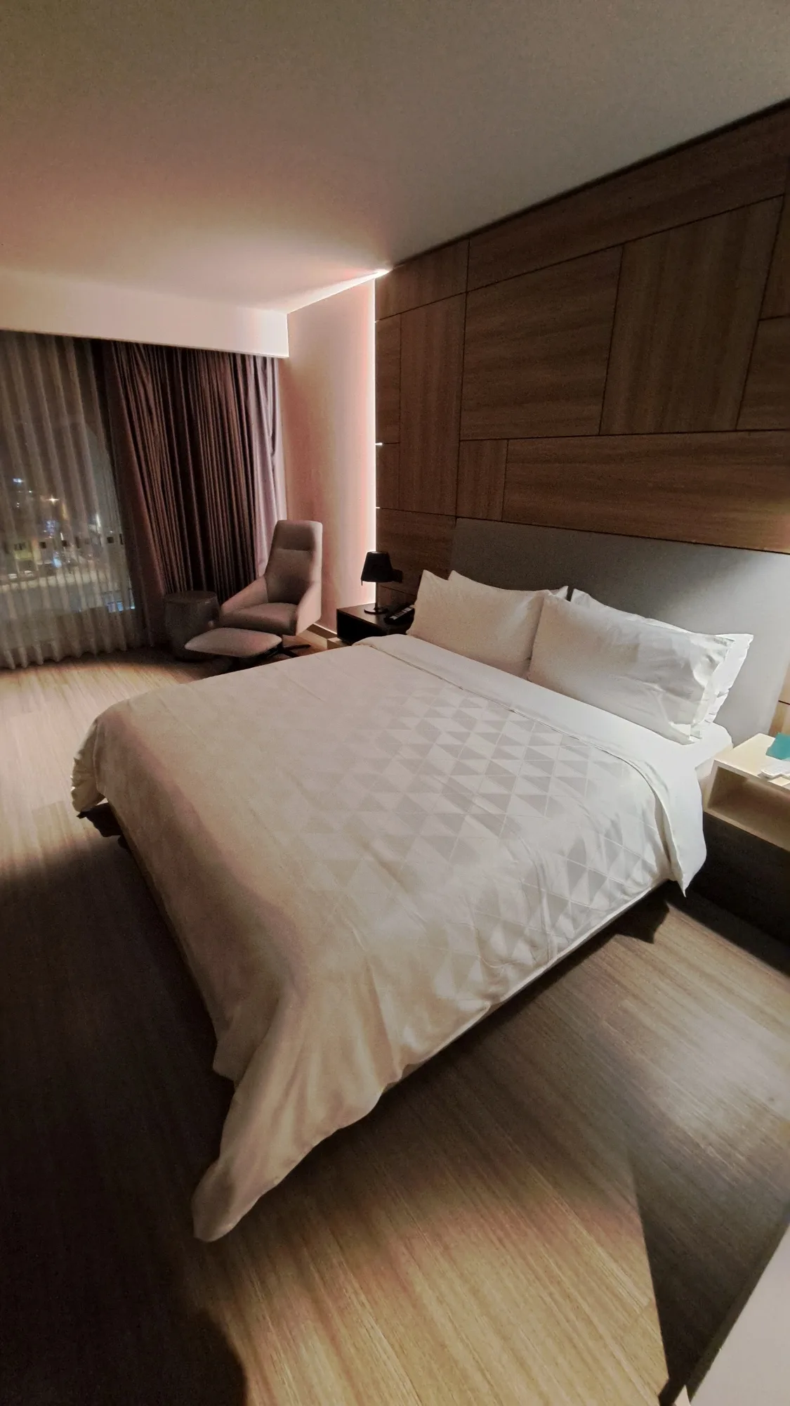 Doppelbett im Hotelzimmer mit Holzverkleidung und grauem Vorhang