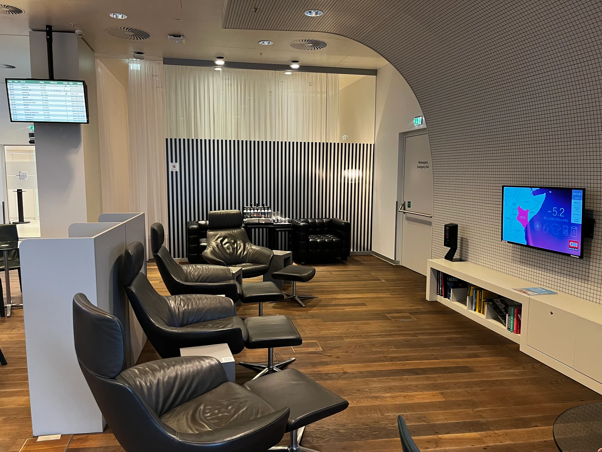 Lounge mit Sesseln und Fernseher im Flughafen Wien