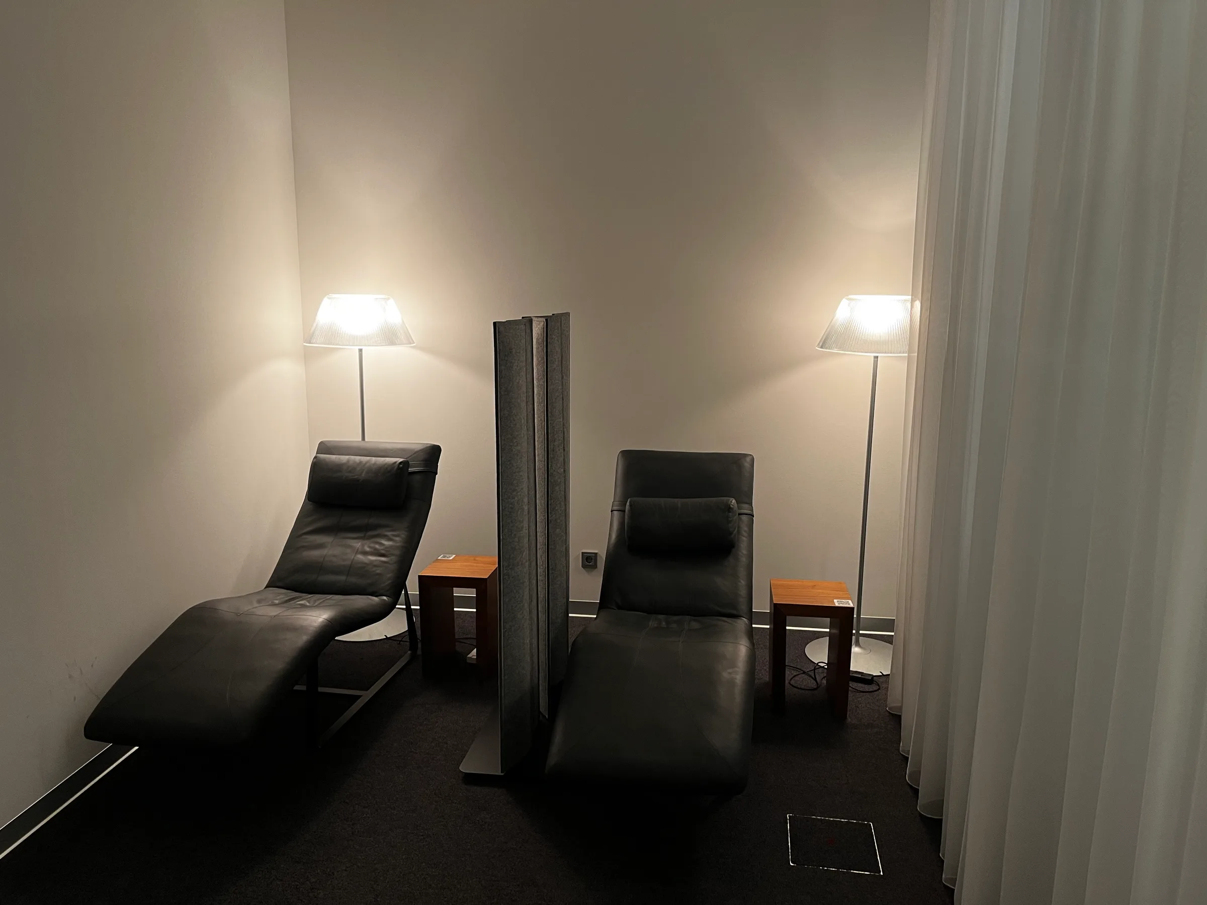 Zwei schwarze Liegestühle vor einer Wand mit zwei Stehlampen