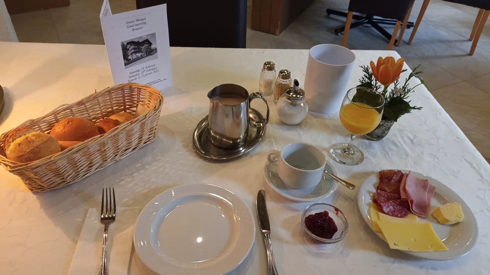 Frühstückstisch mit Brotkorb, Milchkrug, Kaffee, Orangensaft und Käse mit Wurst