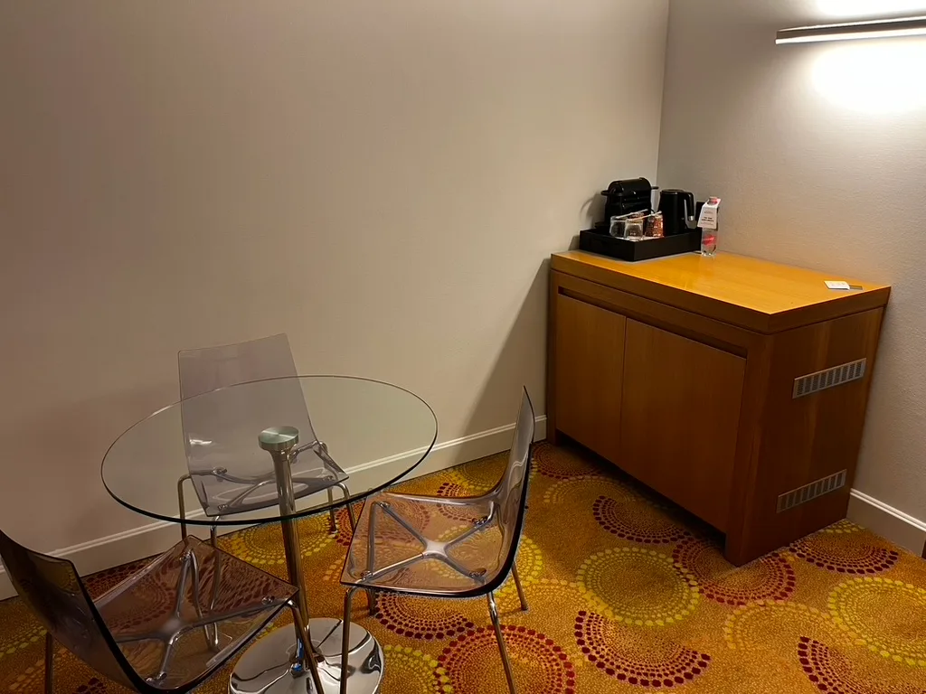 Hotelzimmer mit runder Glas-Tischplatte und transparenten Stühlen