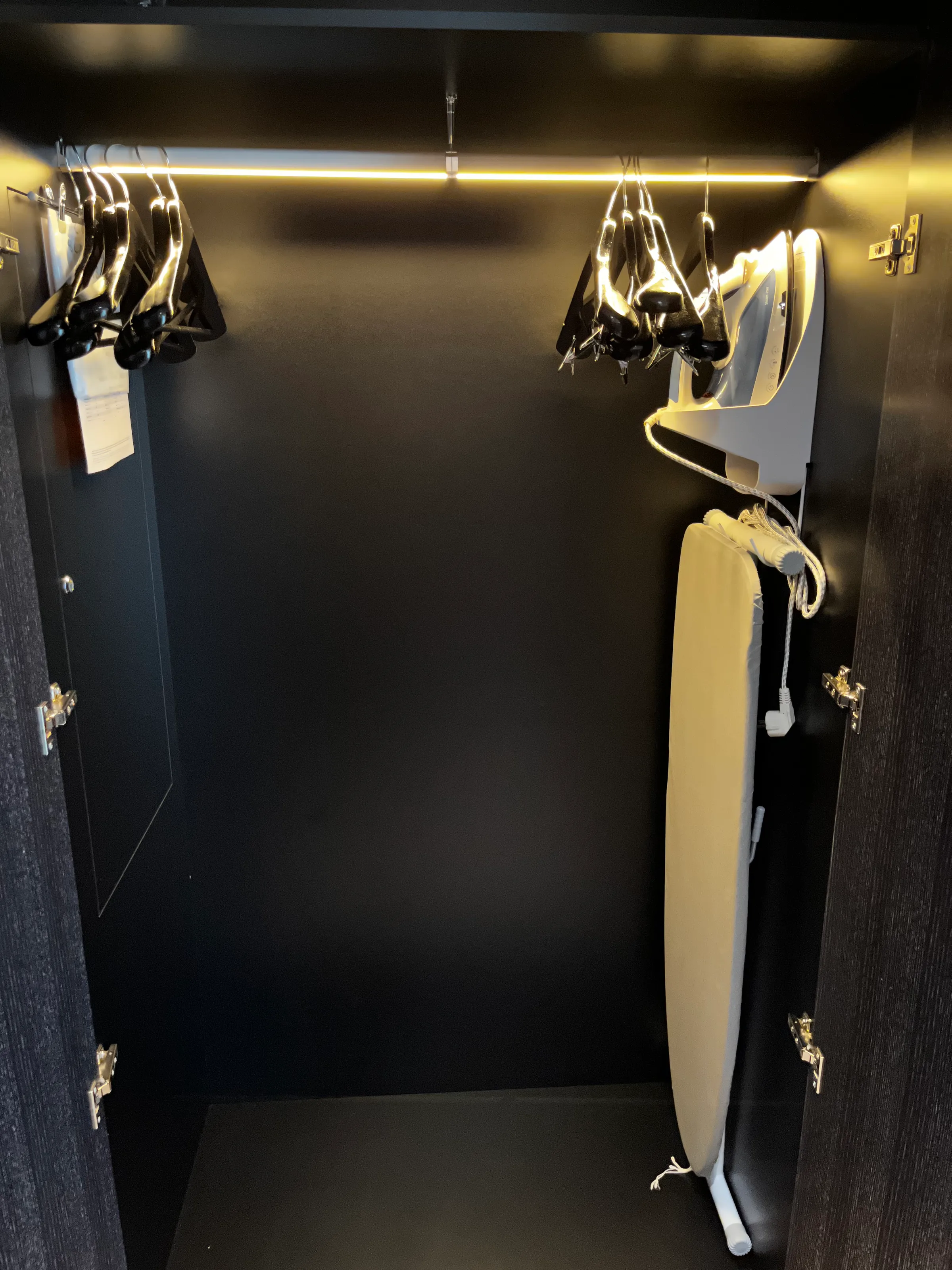 Schrank mit Bügeln und Bügeleisen in dunkler Farbe