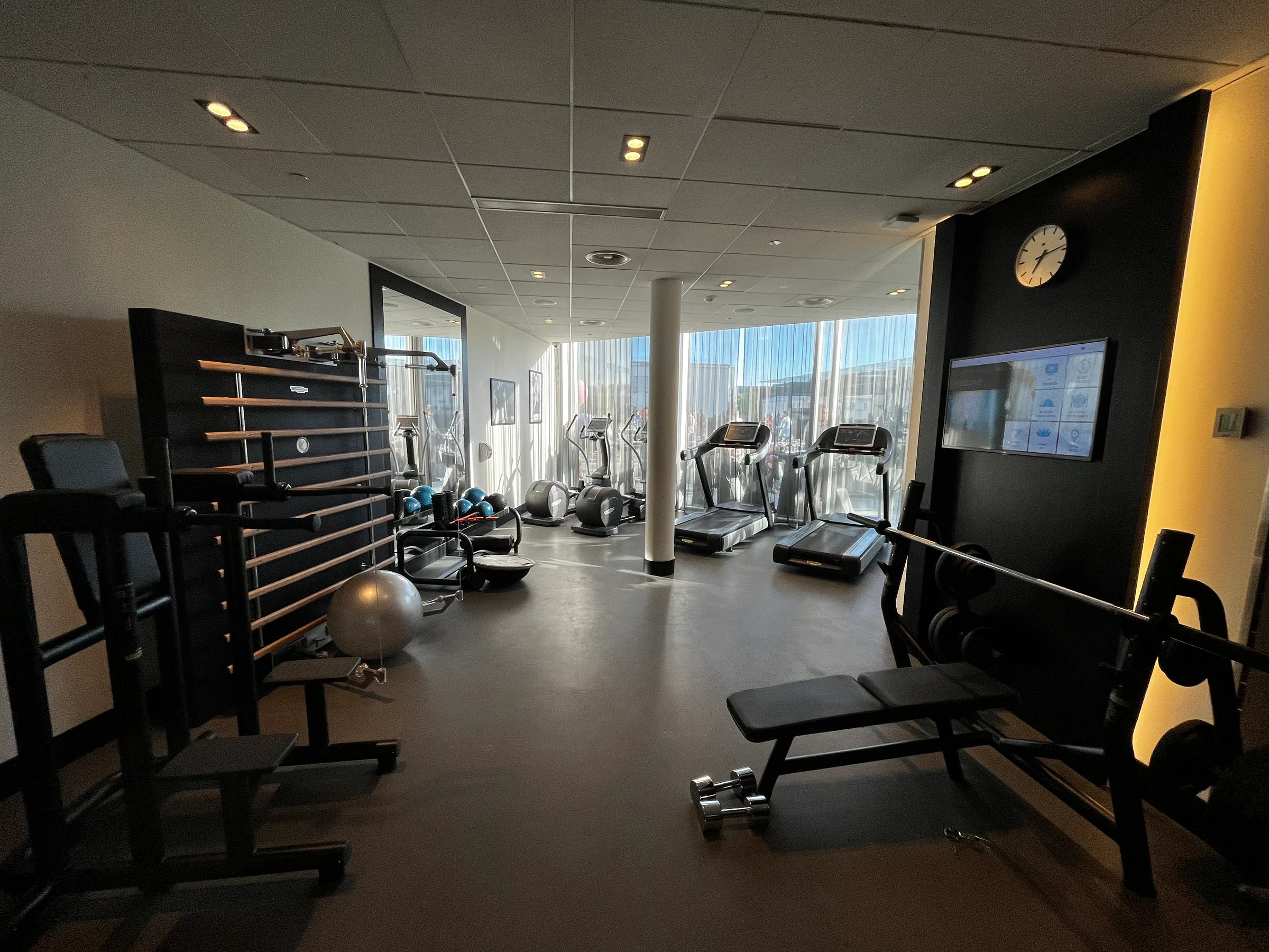 Fitnessraum mit verschiedenen Trainingsgeräten und großen Fenstern