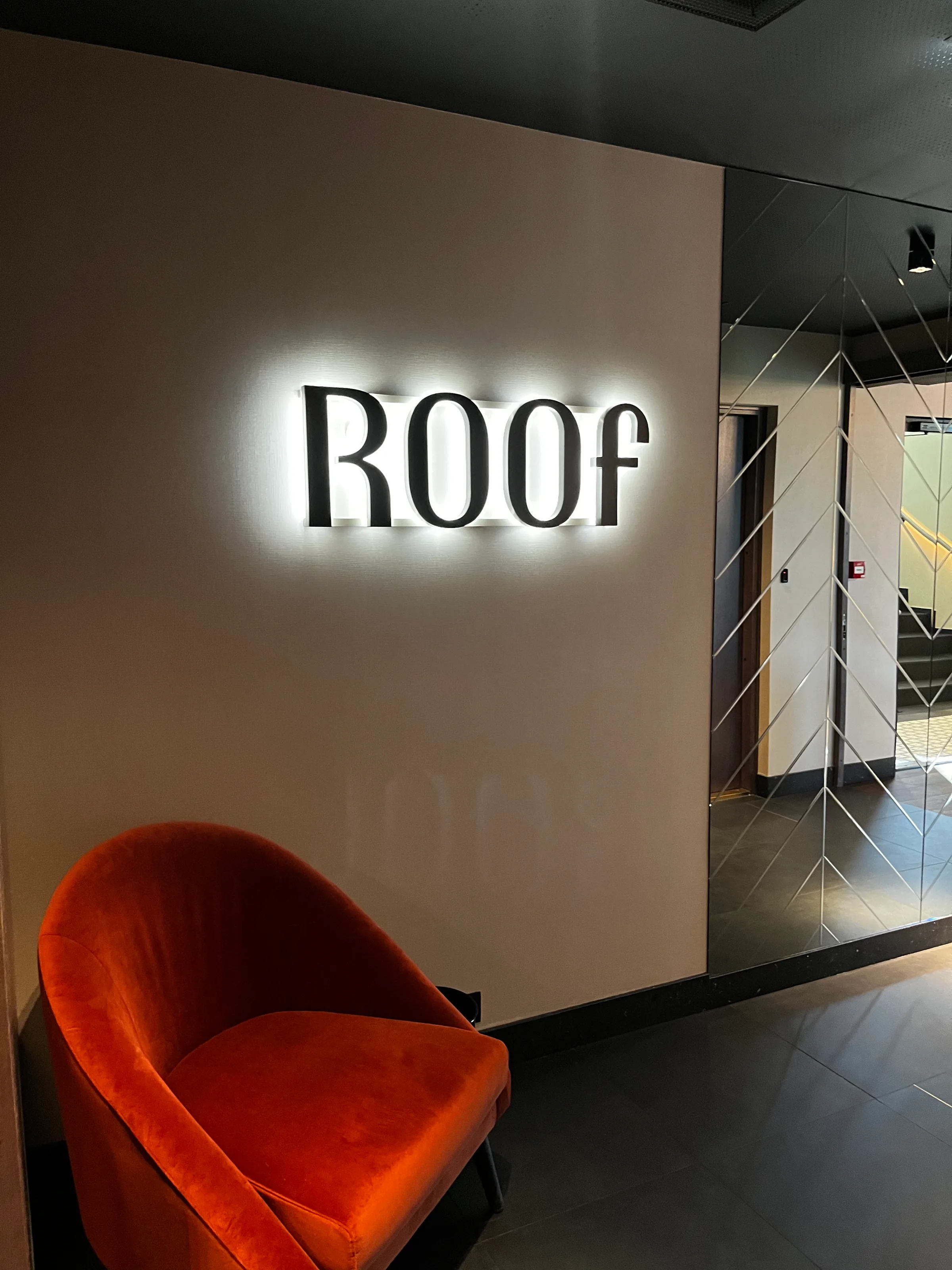 Lobby mit Sitzmöbeln und beleuchtetem Logo 'ROOF'