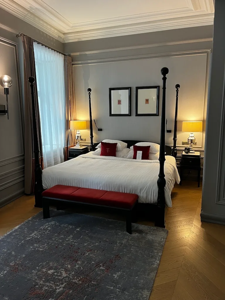 Hotelzimmer mit Doppelbett und rotem Sitzbank vor grauem Teppich