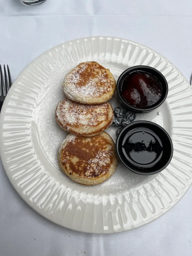 Drei Pfannkuchen mit Puderzucker auf einem Teller mit Marmelade und Sirup