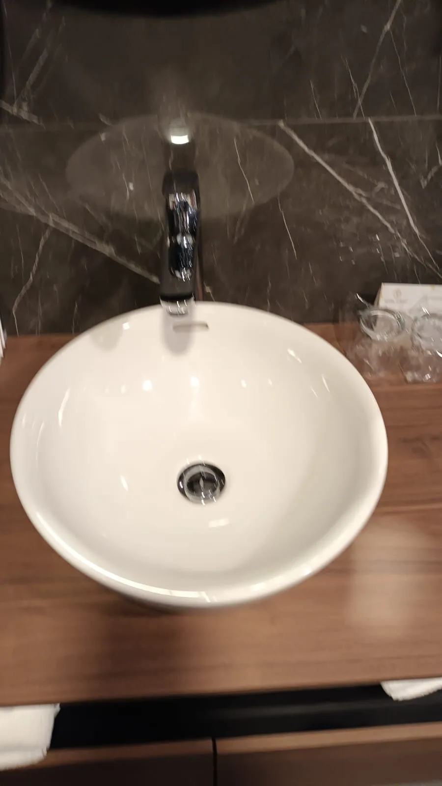 Waschbecken auf Holzunterschrank mit Marmorwand im Hintergrund