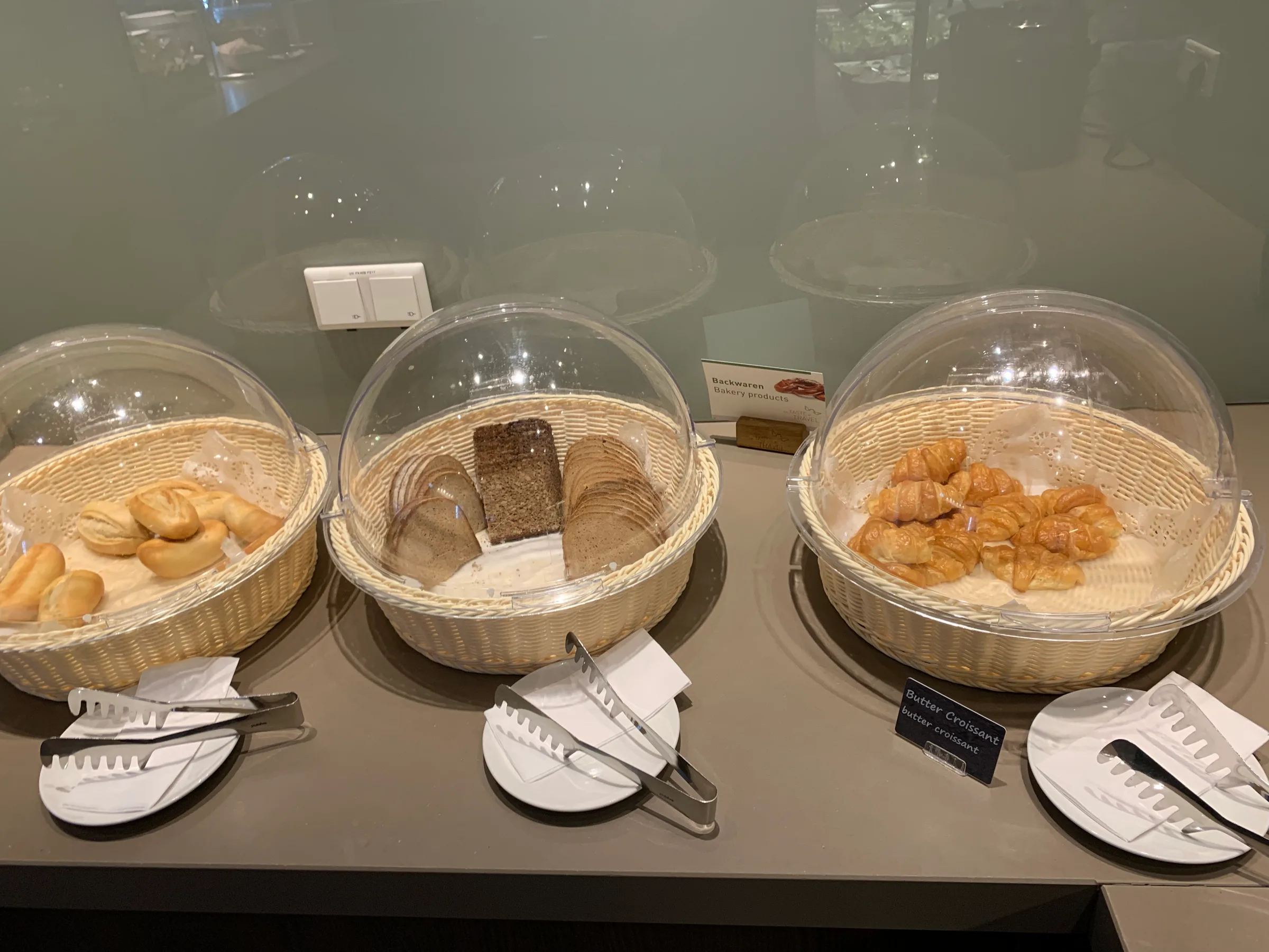 Drei Körbe mit verschiedenen Brotsorten und Buttercroissants auf einem Tisch.