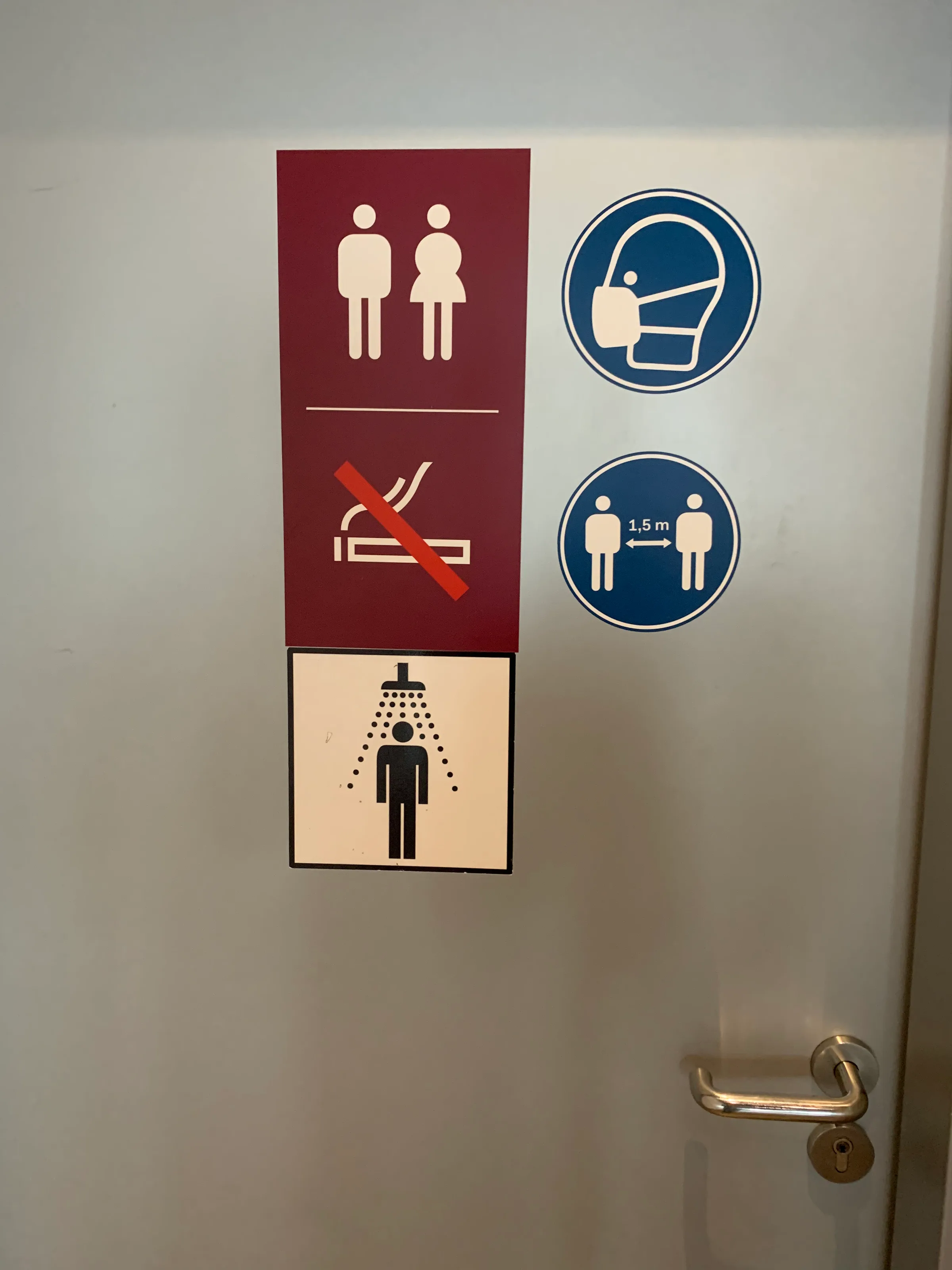Tür mit Toiletten- und Dusch-Symbolen sowie Masken- und Abstands-Aufklebern