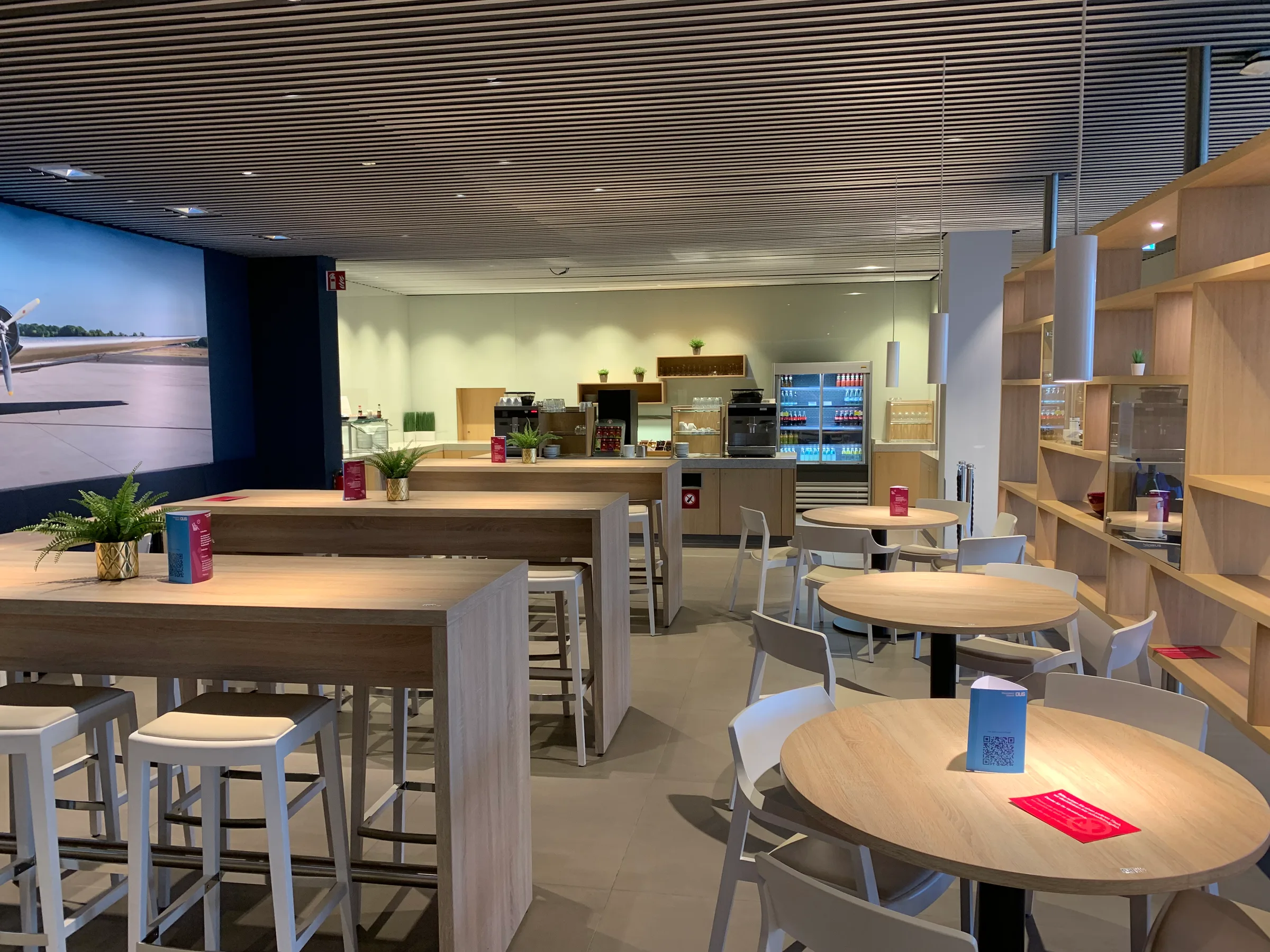 Lounge mit Holztischen und Stühlen, Kaffeeautomaten und Getränkekühlschränken