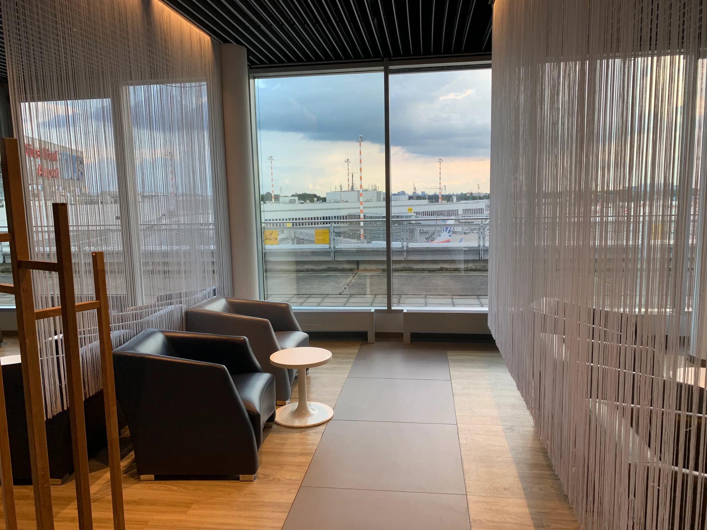 Lounge mit Sesseln und Tisch vor Fenster mit Flughafenblick