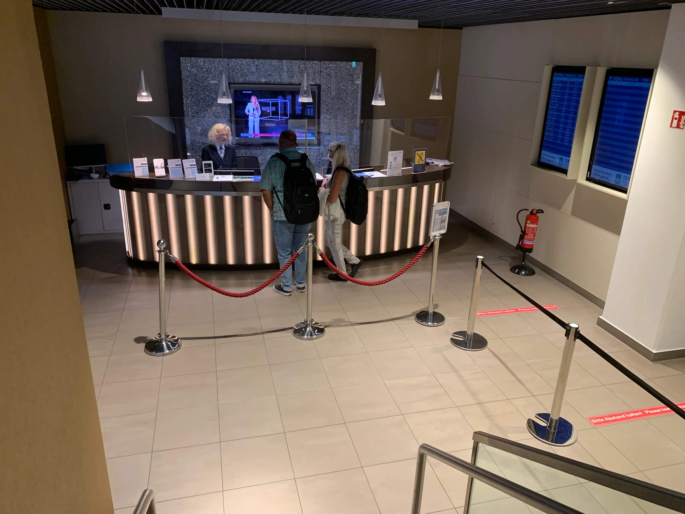 Rezeption mit Fernseher und Personen im Flughafenlounge während Corona