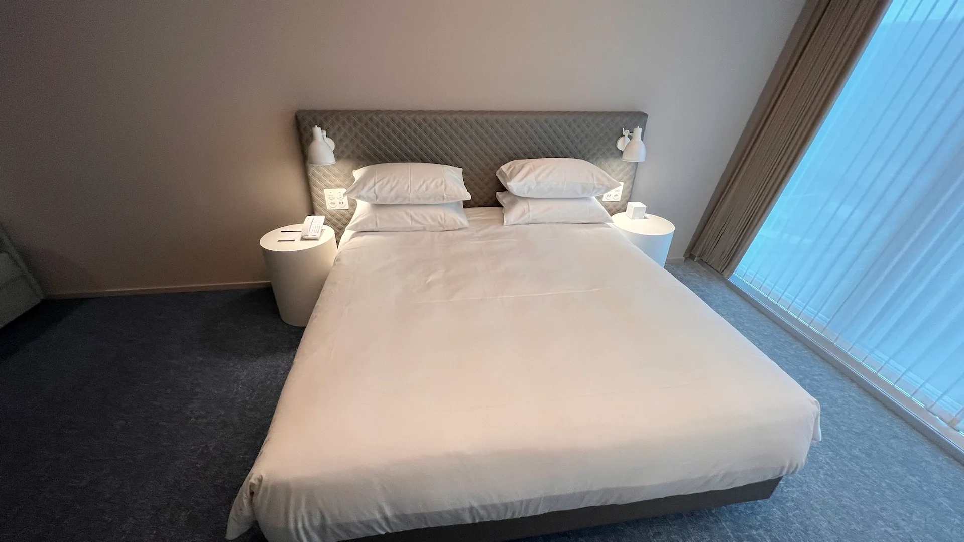 Hotelzimmer mit Doppelbett und Nachttischen in Grautönen