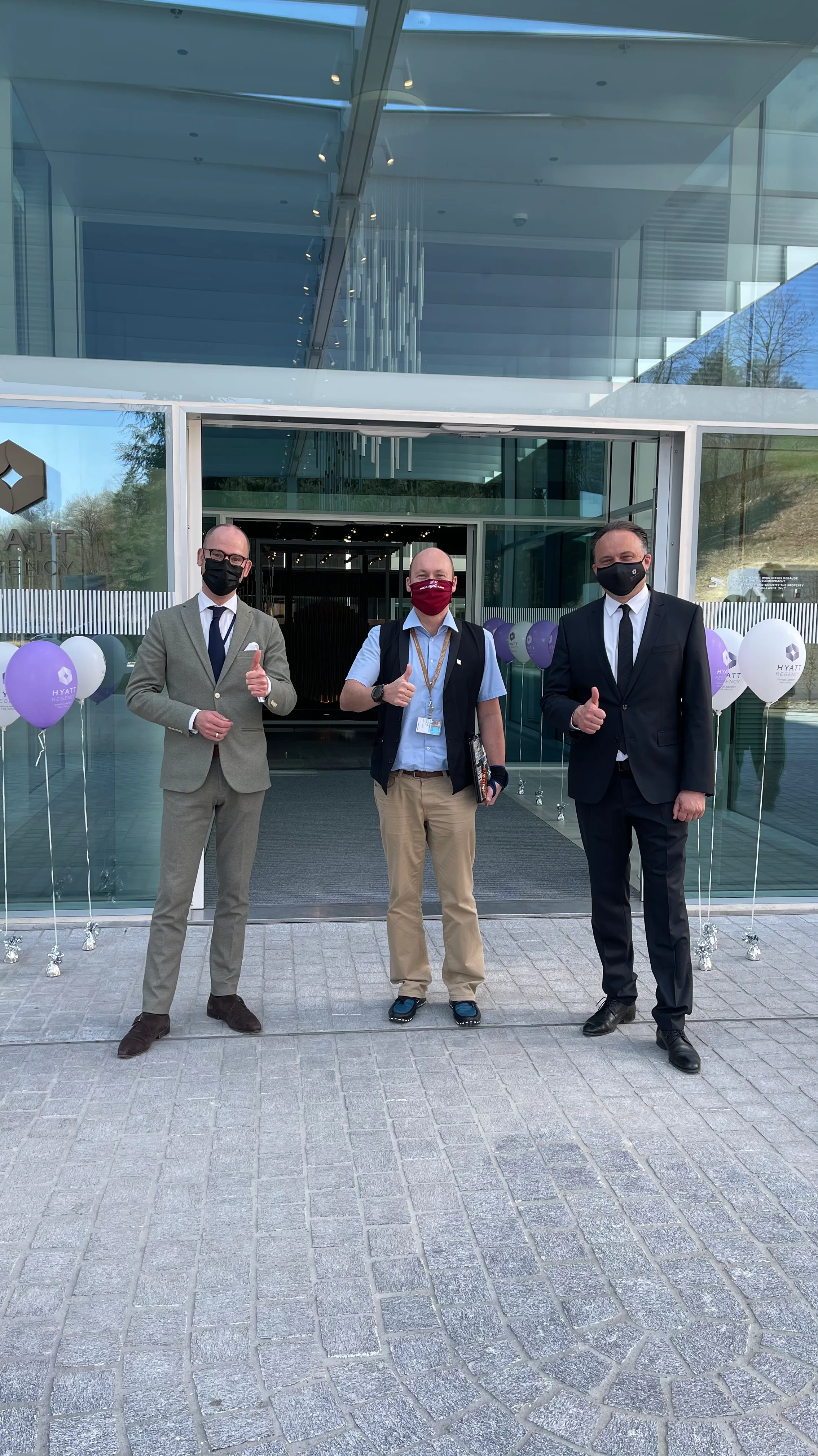 Drei Männer mit Gesichtsmasken vor einem modernen Gebäude