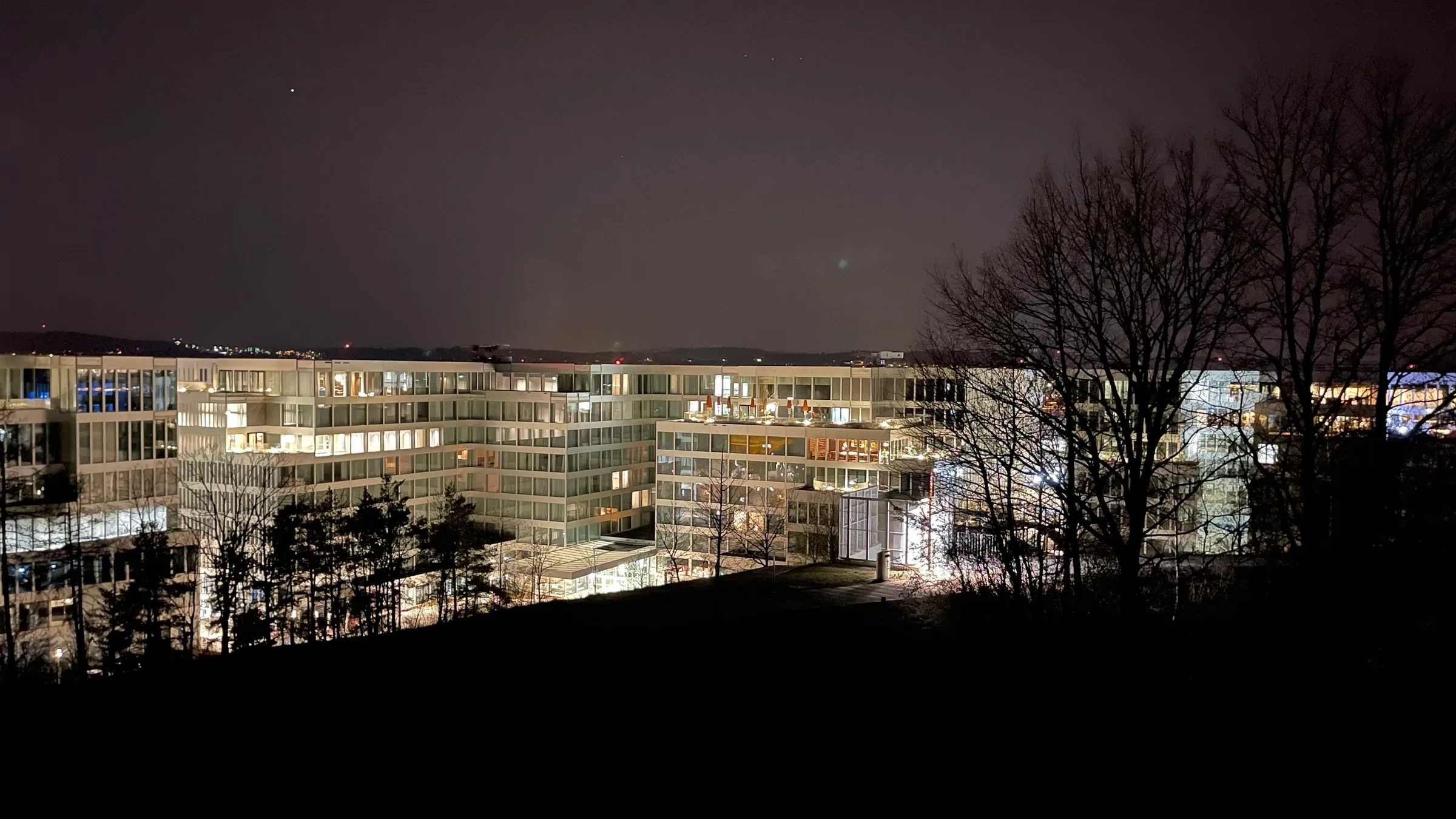 Beleuchtete Hotelgebäude bei Nacht mit Bäumen im Vordergrund