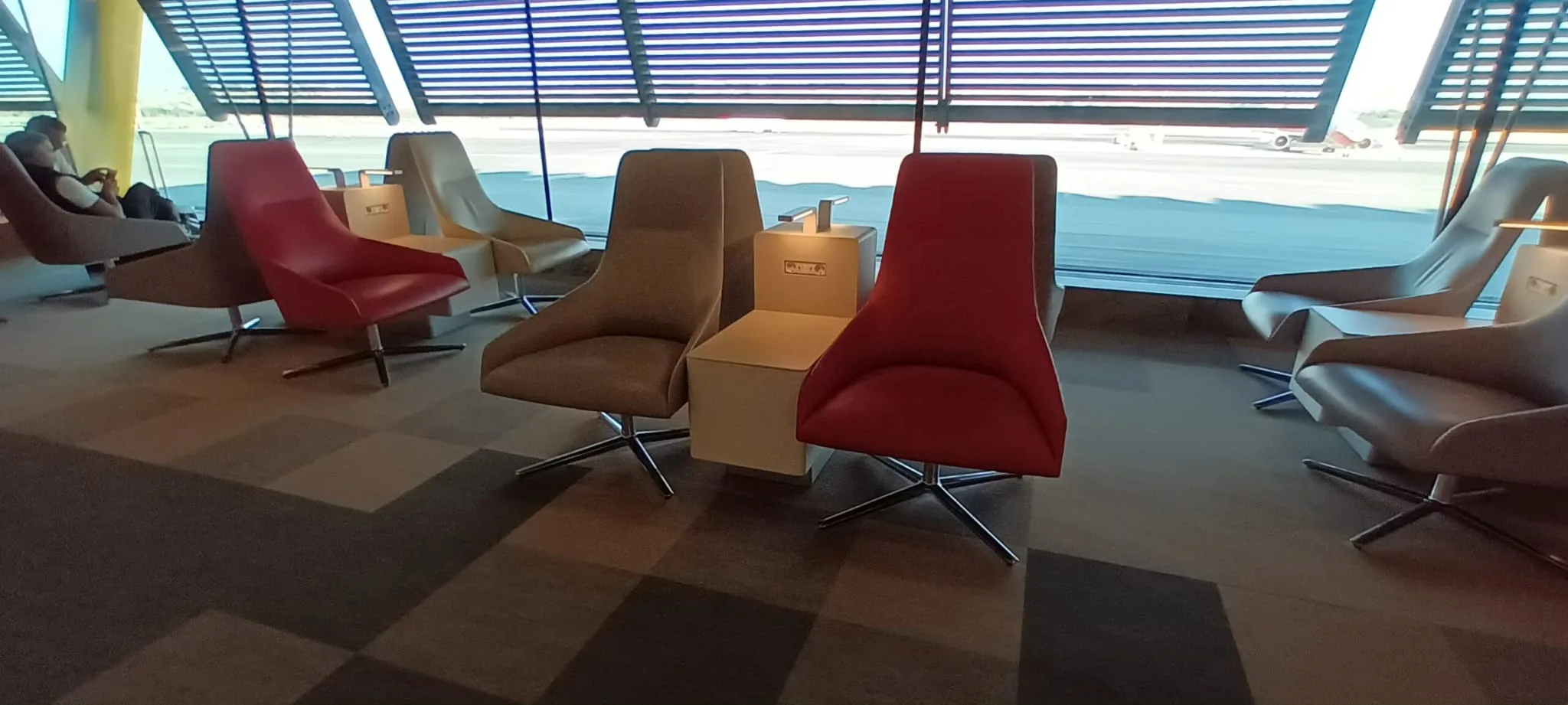 Rote und beige Sessel in einem Loungesaal mit Blick auf den Flughafen