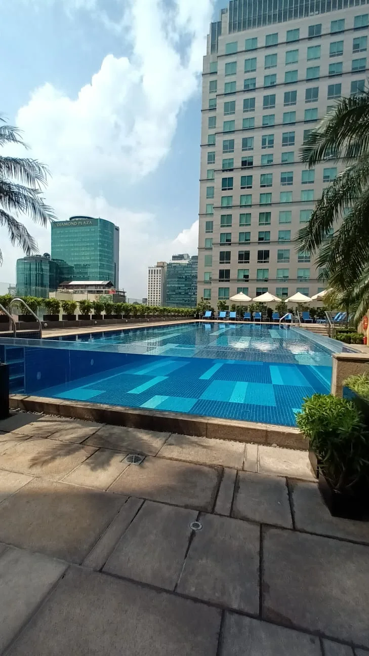 Hotelpool mit Liegestühlen und Palmen im Vordergrund