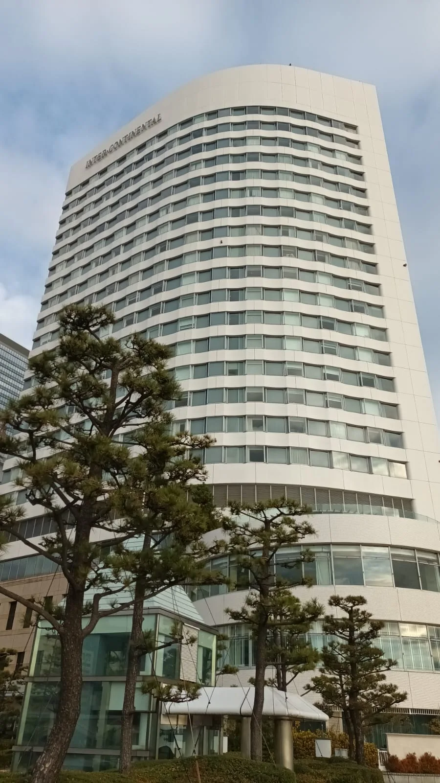 Weißes Hochhaus mit geschwungenen Fassaden und Bäumen im Vordergrund