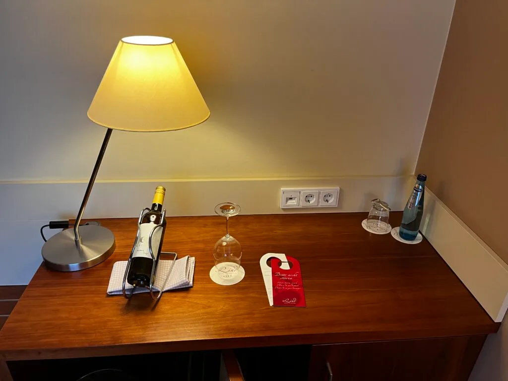 Hotelzimmer mit Nachttischlampe, Flasche Wein und Weinglas
