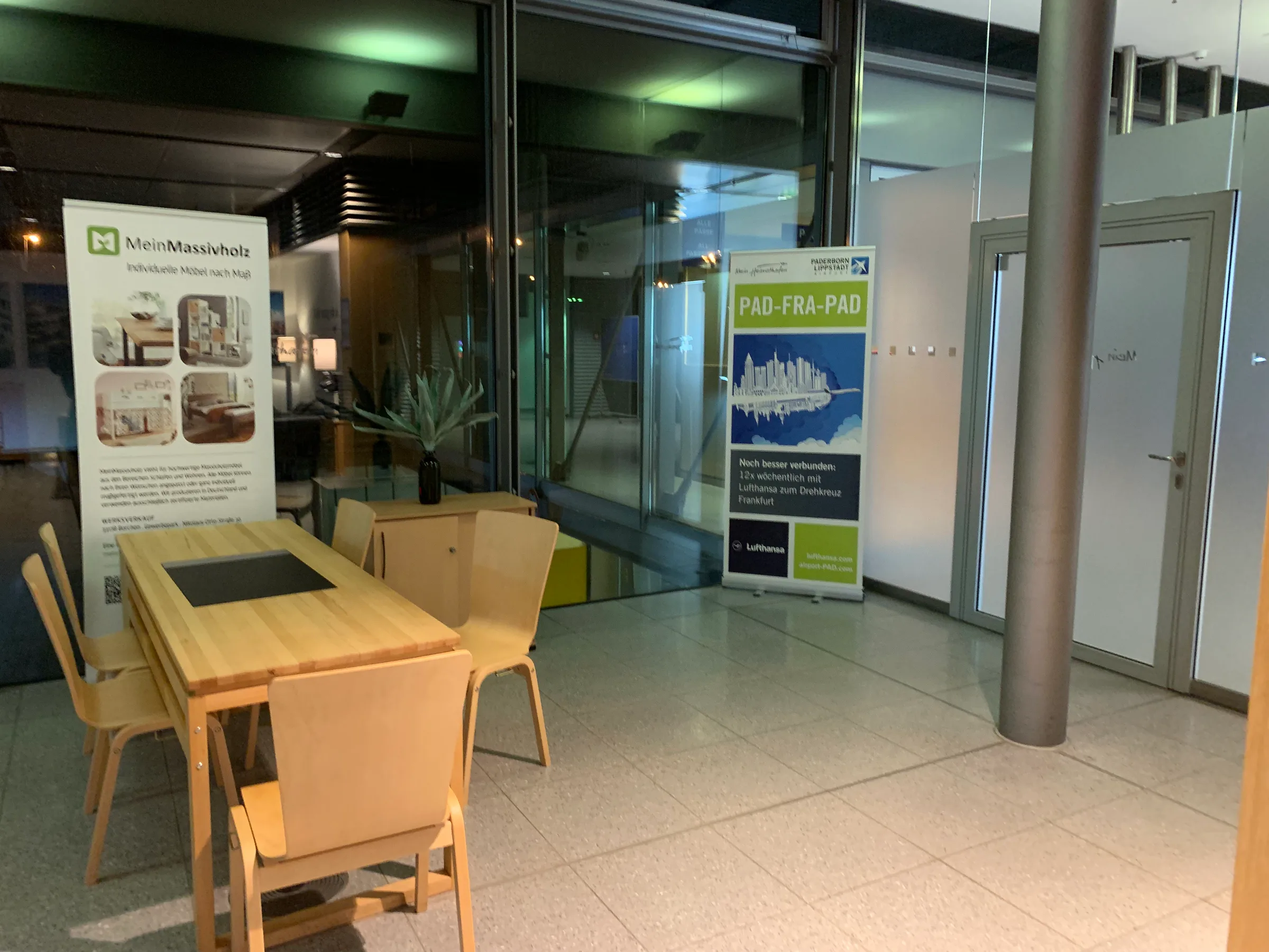 Lounge mit Tisch und Stühlen sowie Werbetafeln für Möbel und Lufthansa