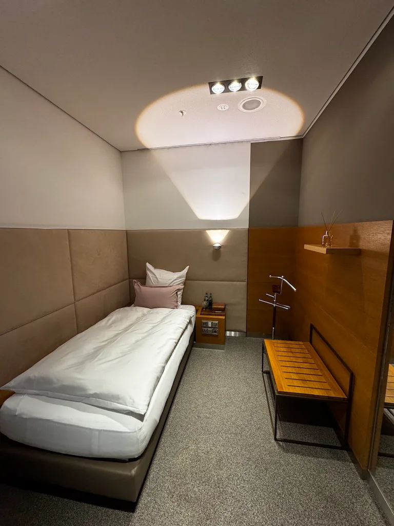 Einzelbett im First Class Lounge mit grauem Teppich und Holzmöbeln