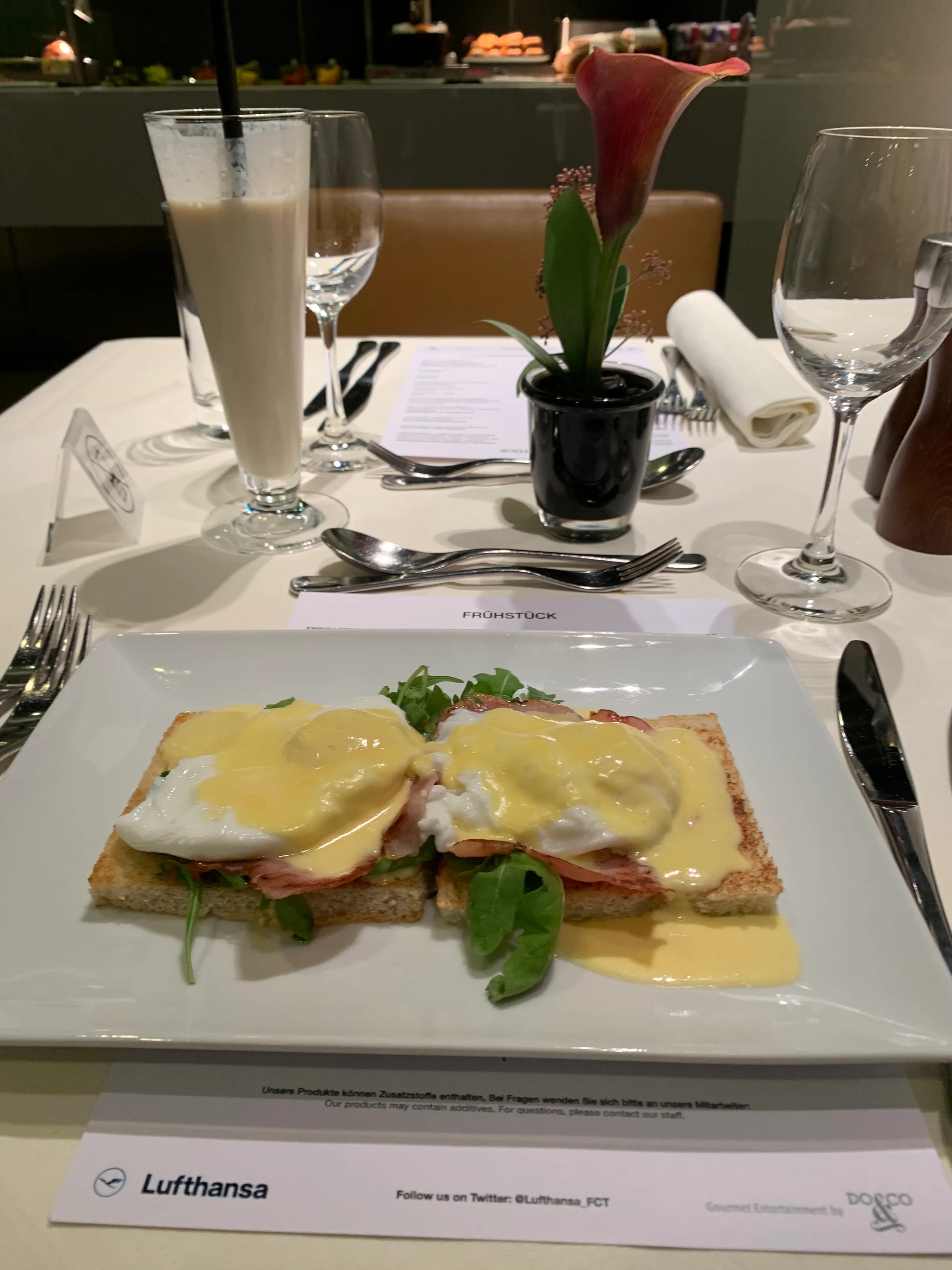 Eierbrötchen mit Speck und Ei auf einem Teller mit Milchshake und Blume