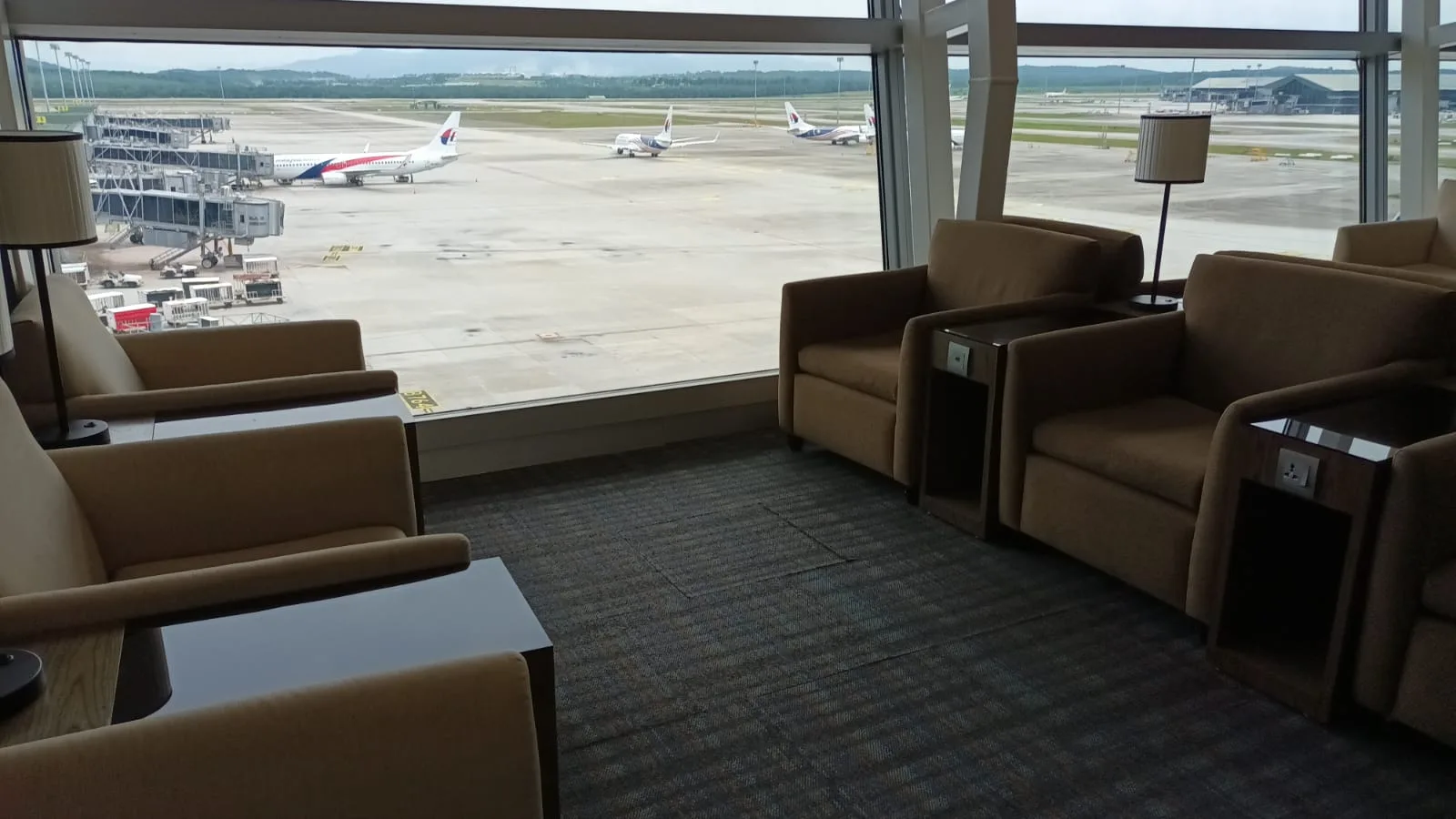 Lounge mit Sesseln und Tischen vor Flughafenfenster