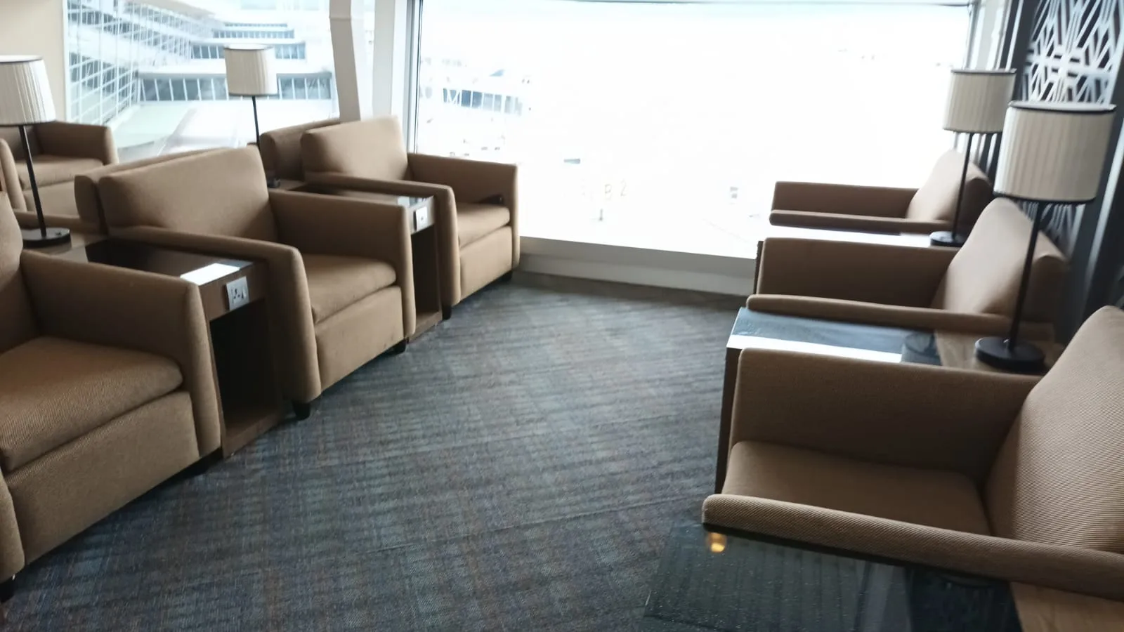 Lounge mit Sesseln und Tischen vor Fensterfront