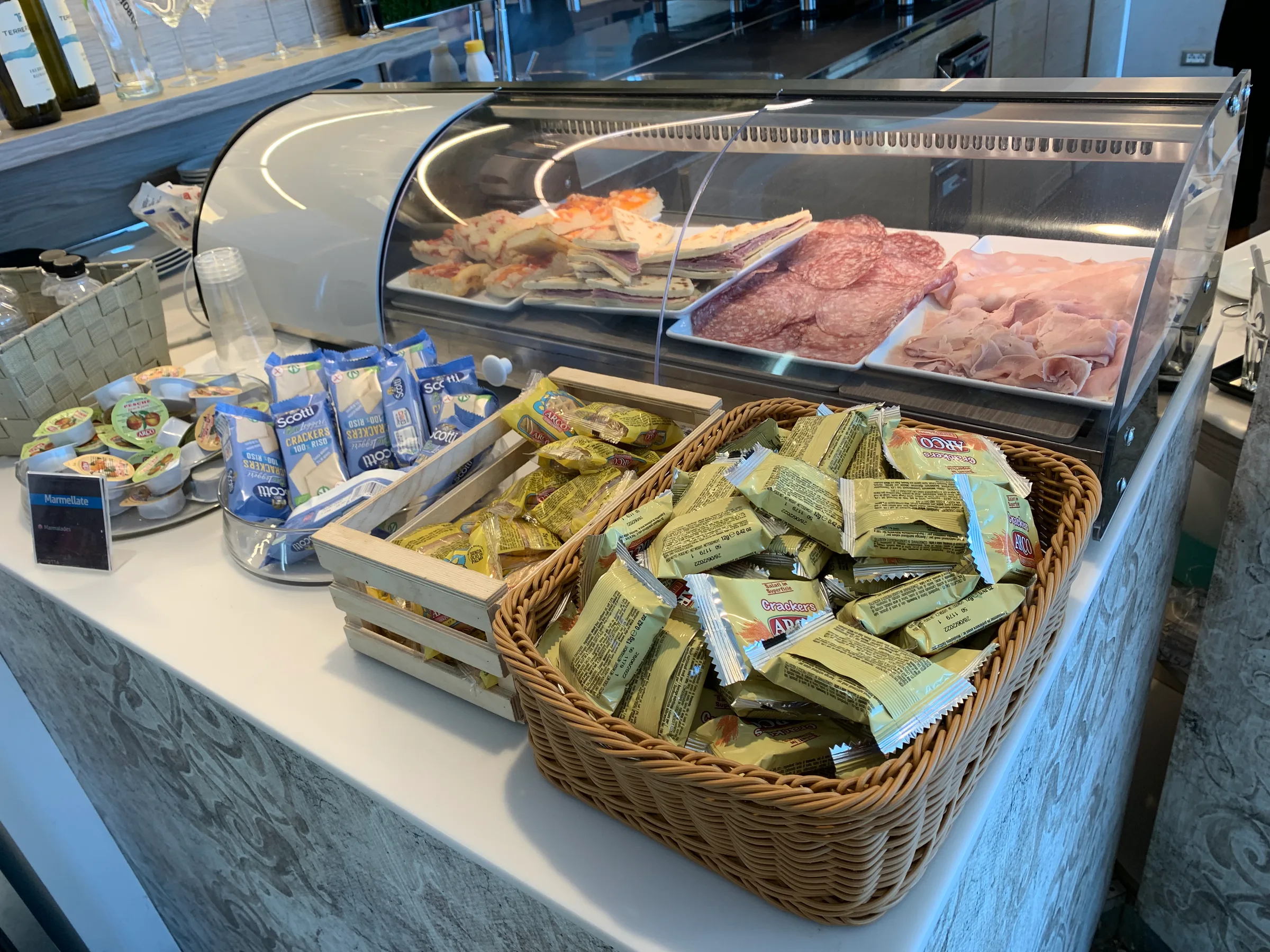 Geschnittene Wurst und Käse im Vitrinenschrank neben Keksen und Snacks in Körben