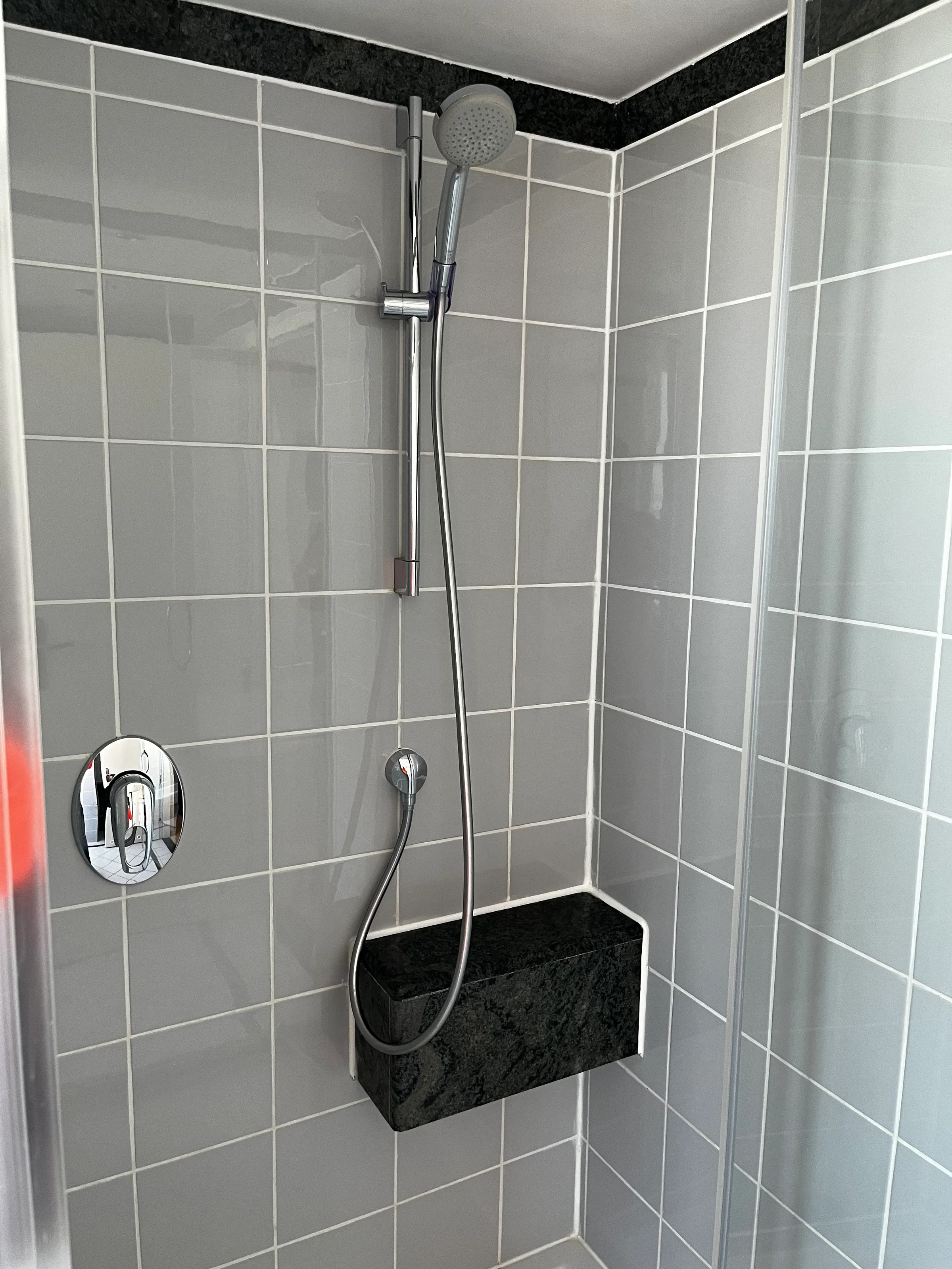 Duschbereich mit Handbrause und Regal in grauen Fliesen