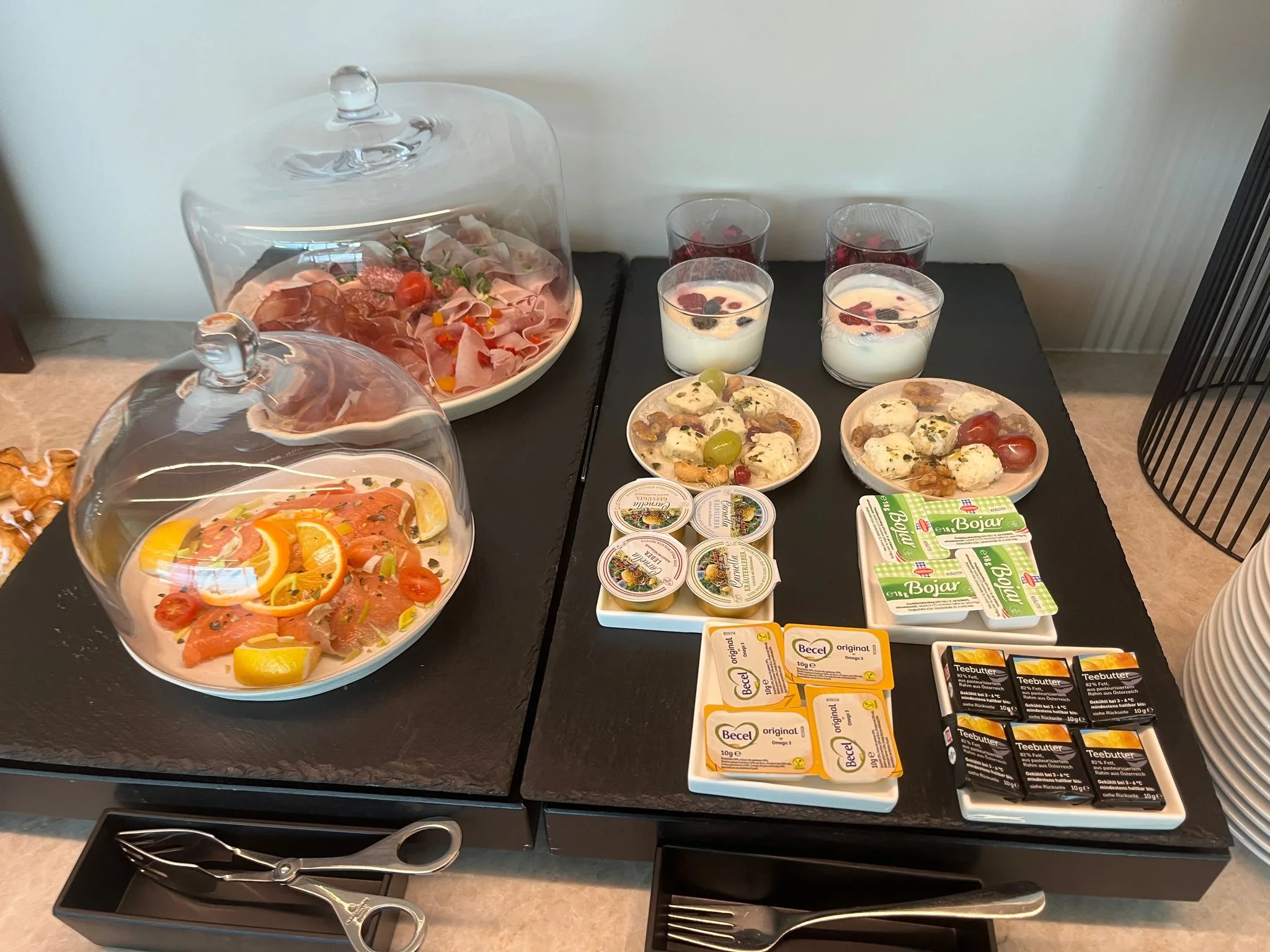 Frühstückstablett mit Salat, Käse und Früchten unter Glasbehältern