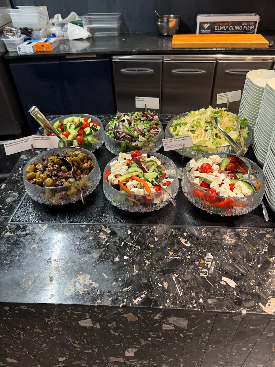 Salatbuffet mit verschiedenen Salaten und Oliven auf einem schwarzen Marmoruntergrund