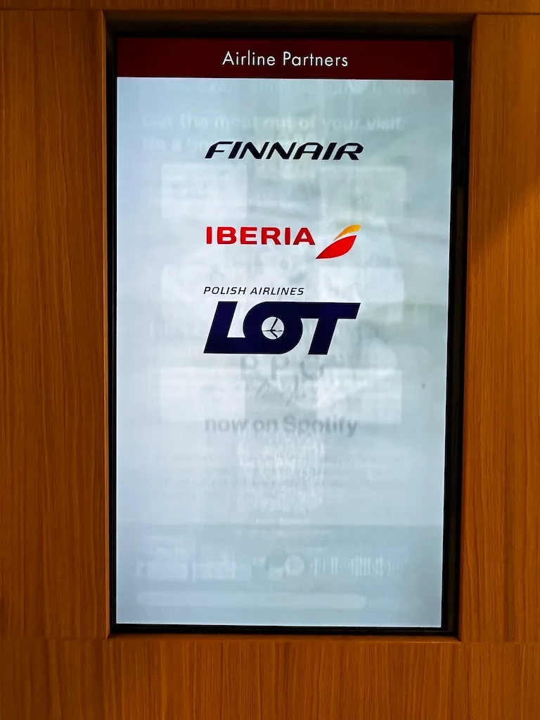 Flughafenschild mit Logos von Finnair, Iberia und LOT