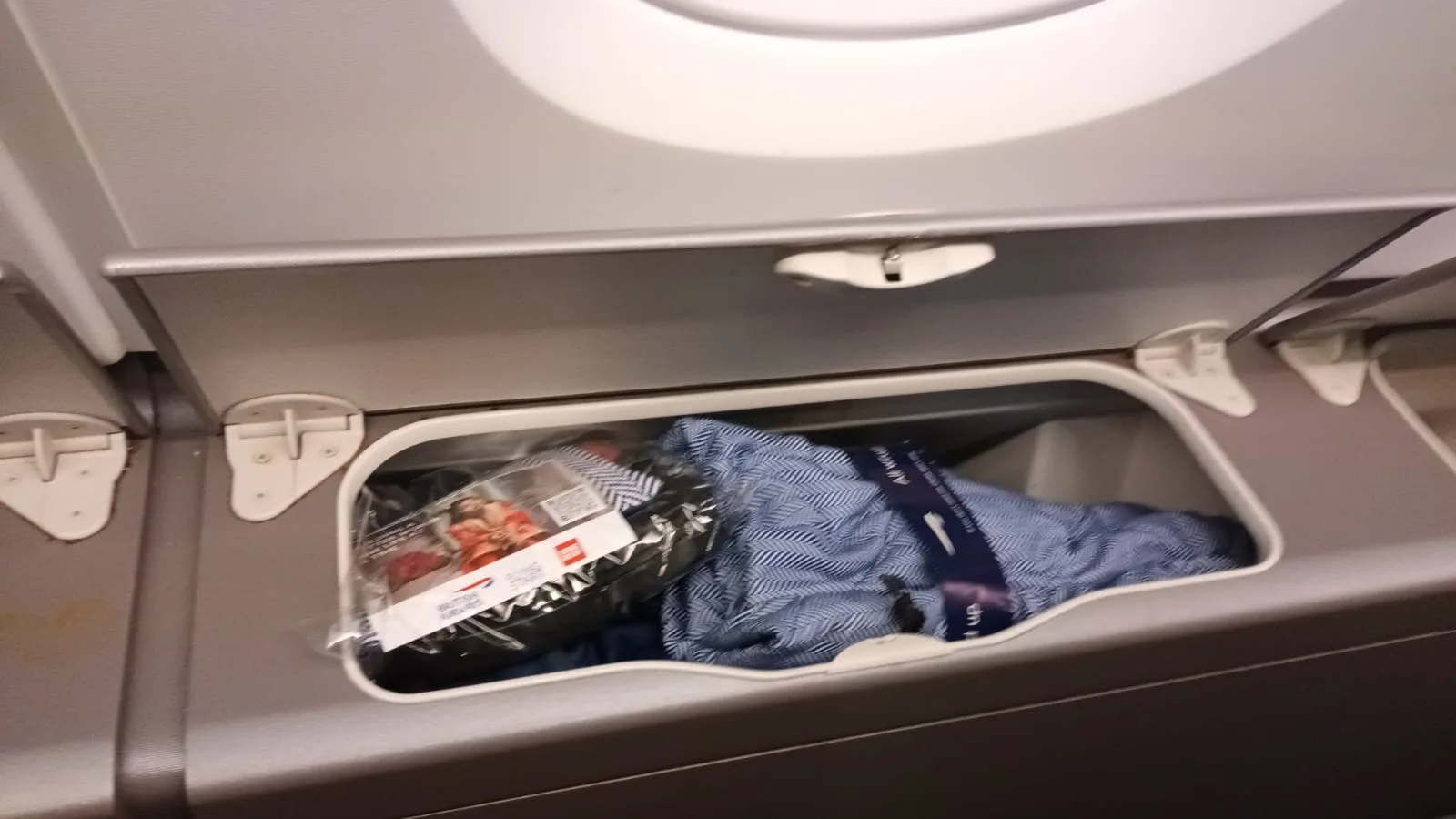 Gepäckbehälter im Flugzeug mit Kleidungsstück und Verpackung