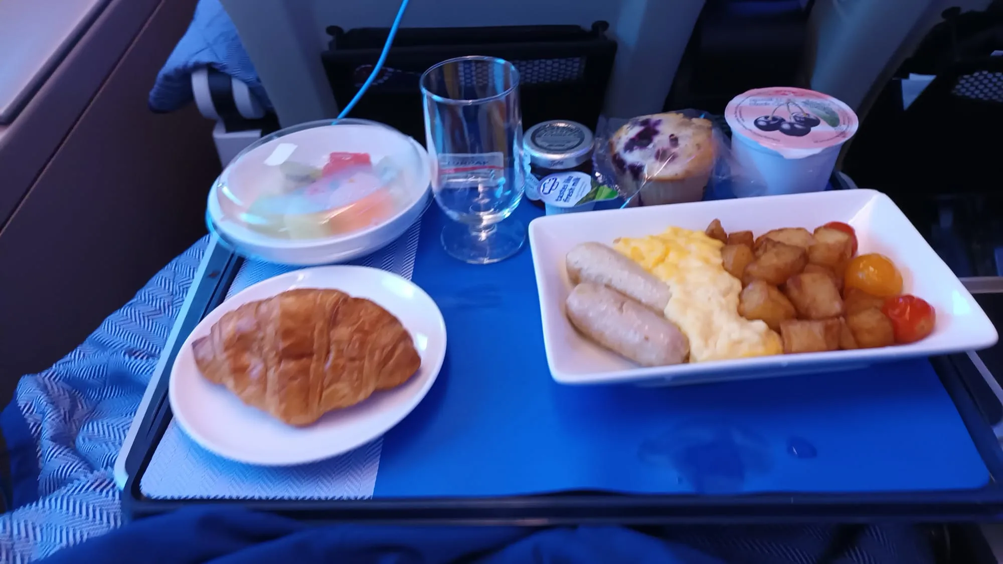Frühstückstablett mit Croissant, Eier, Würstchen und Beeren auf einem Flugzeugtisch