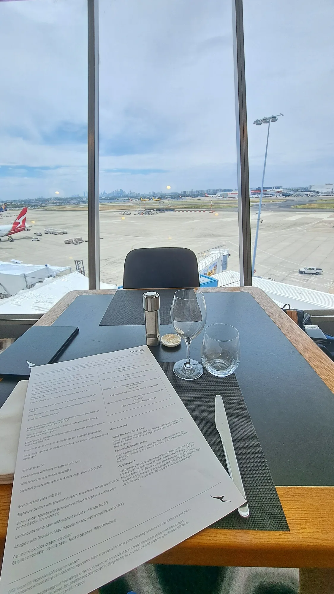 Tisch im Qantas First Lounge mit Menü und Blick auf Flughafen
