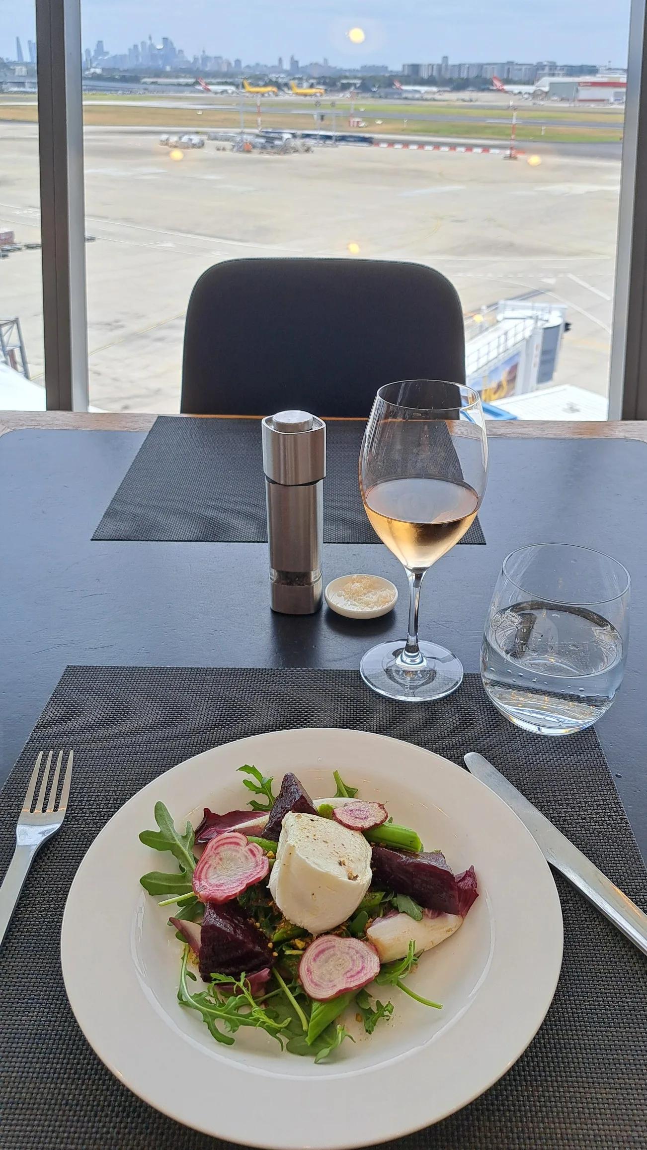 Tisch im Qantas First Lounge mit Salat, Wein und Blick auf Flughafen