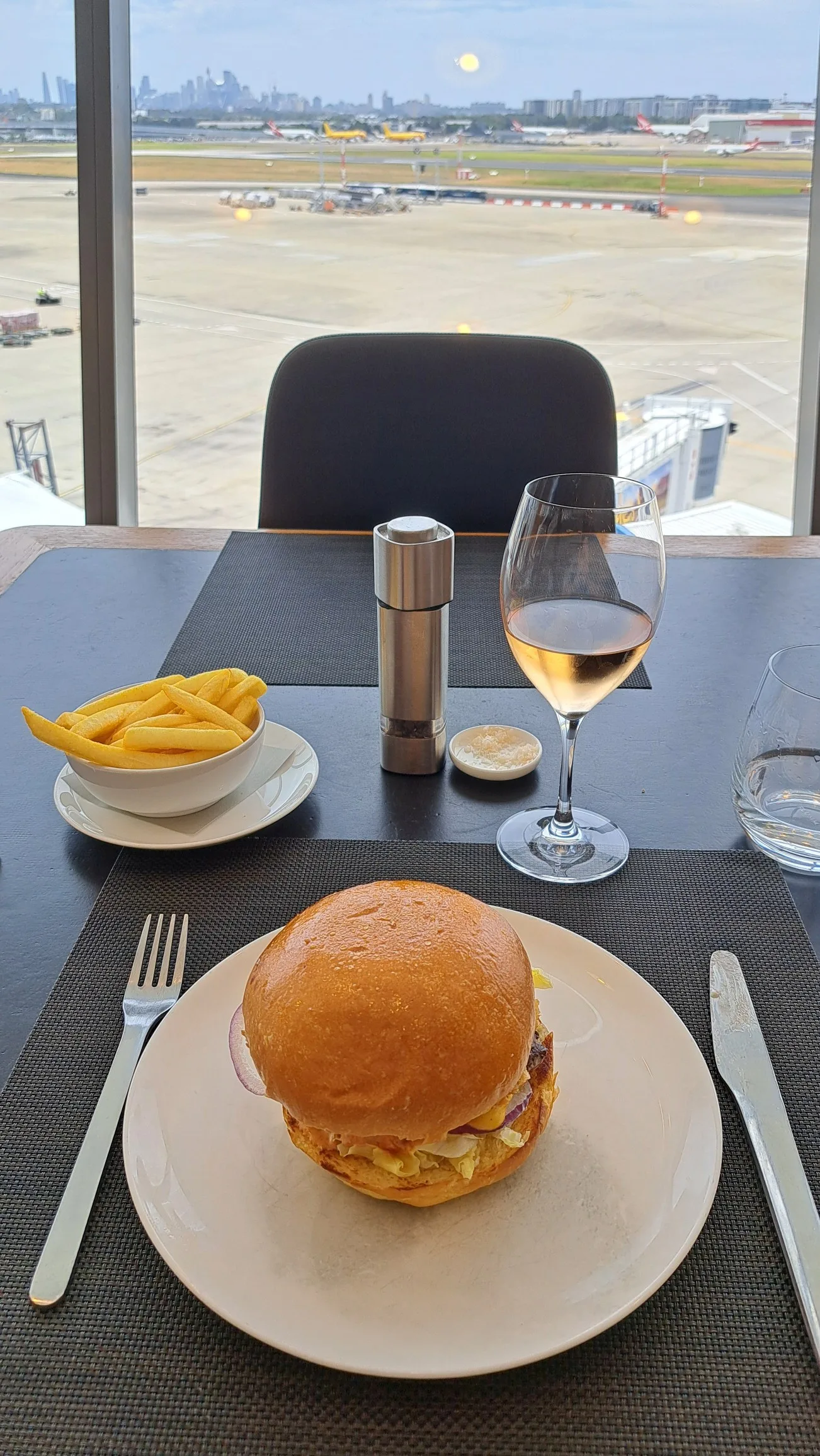 Burger mit Pommes und Weißwein auf Tisch im Flughafenlounge