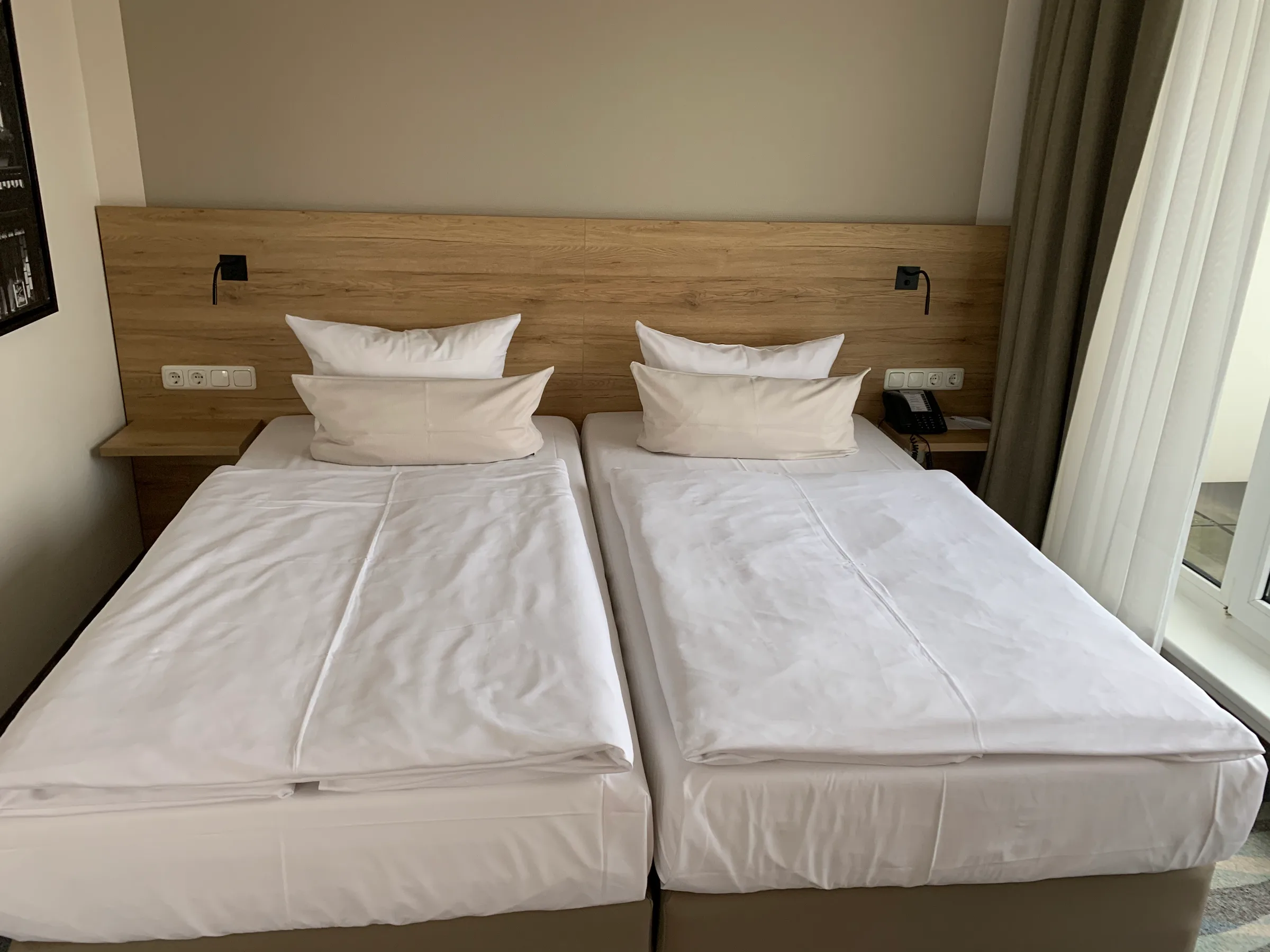 Doppelbett im Hotelzimmer mit Holzbettgestell und grauen Vorhängen