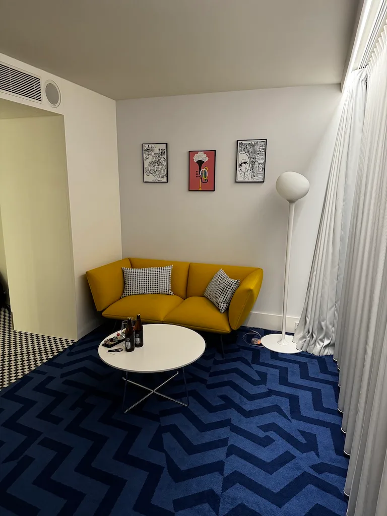 Gelbes Sofa mit Kissen vor blauem Teppich im Hotelzimmer