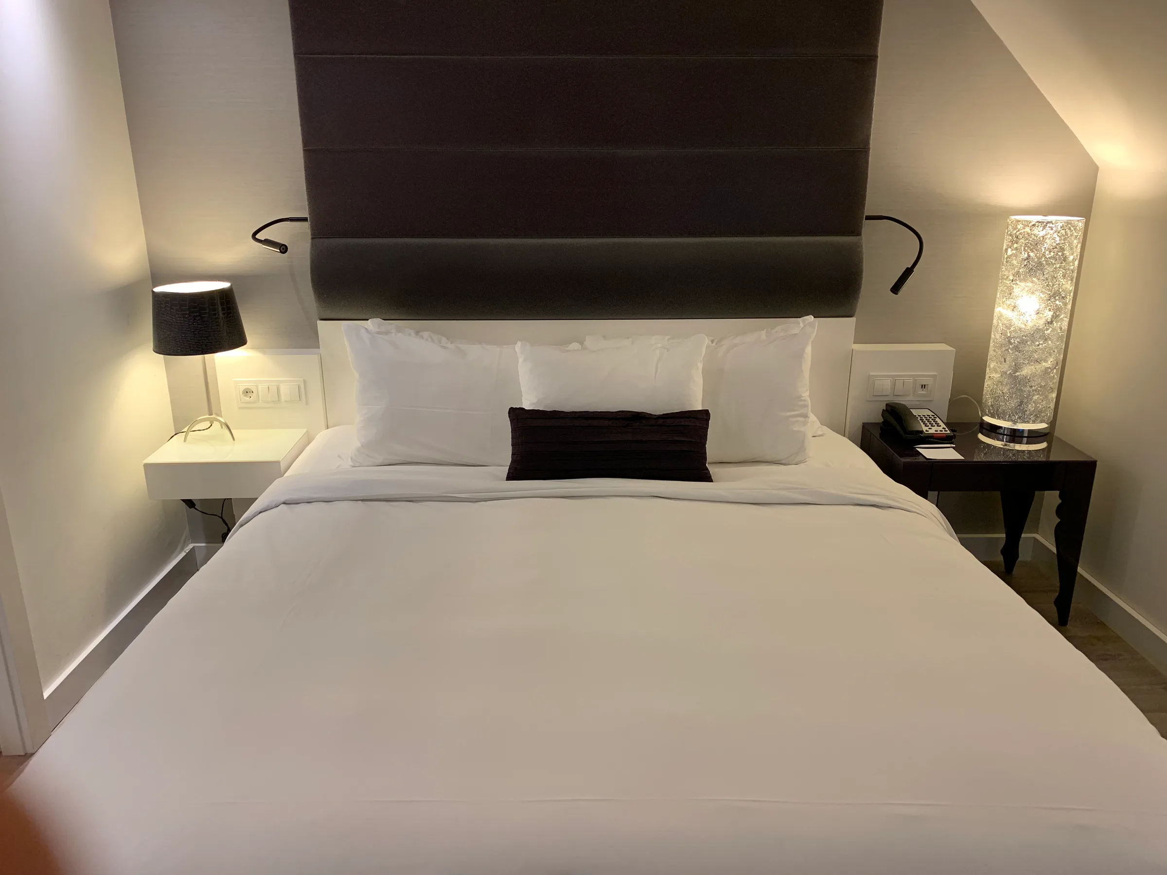 Doppelbett im Hotelzimmer mit grauem Kopfteil und Nachttischen