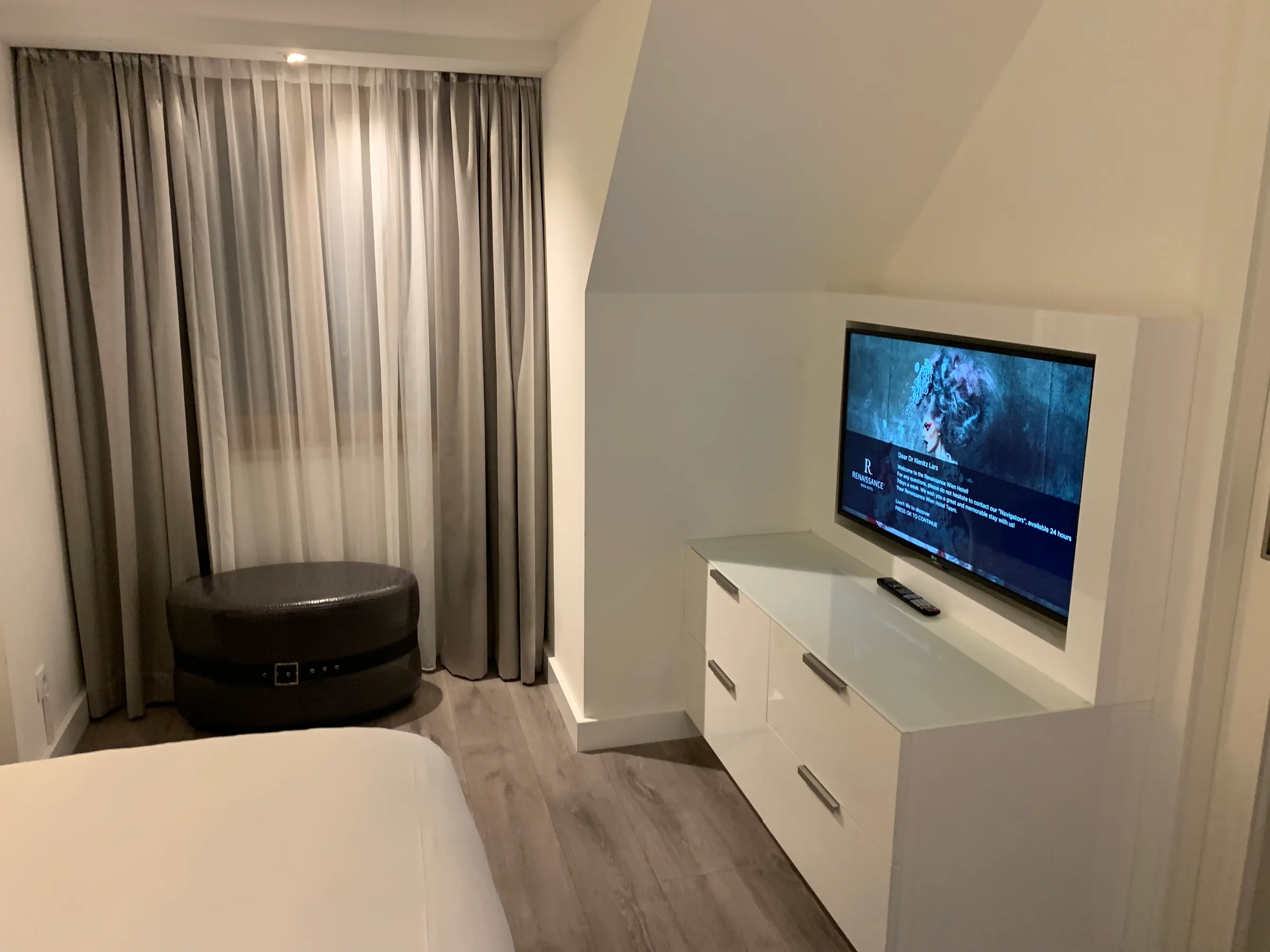 Hotelzimmer mit Bett, Fernseher und Schrank in Grautönen