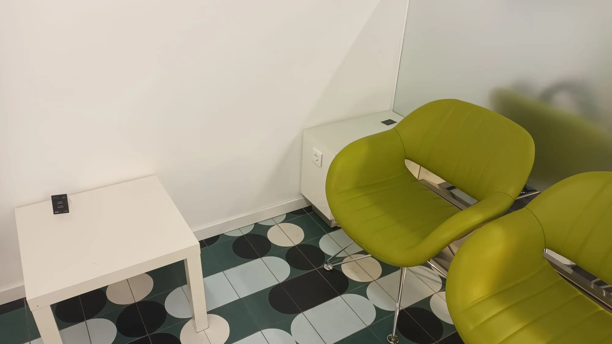 Zwei grüne Stühle vor weißem Tisch in einem Flughafensalon