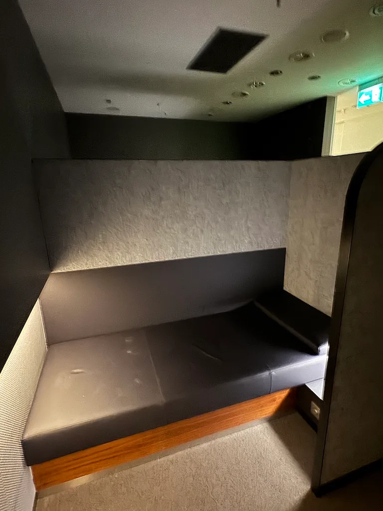 Einzelbett im Flughafen-Senator-Lounge mit grauem Polster und Holzfußbrett