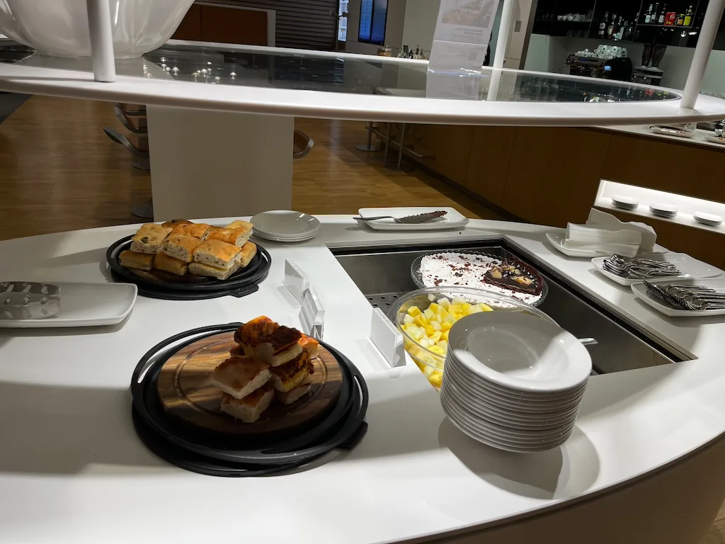 Buffet mit Kuchen, Obst und Brötchen auf einem Flughafen-Lounge-Tisch