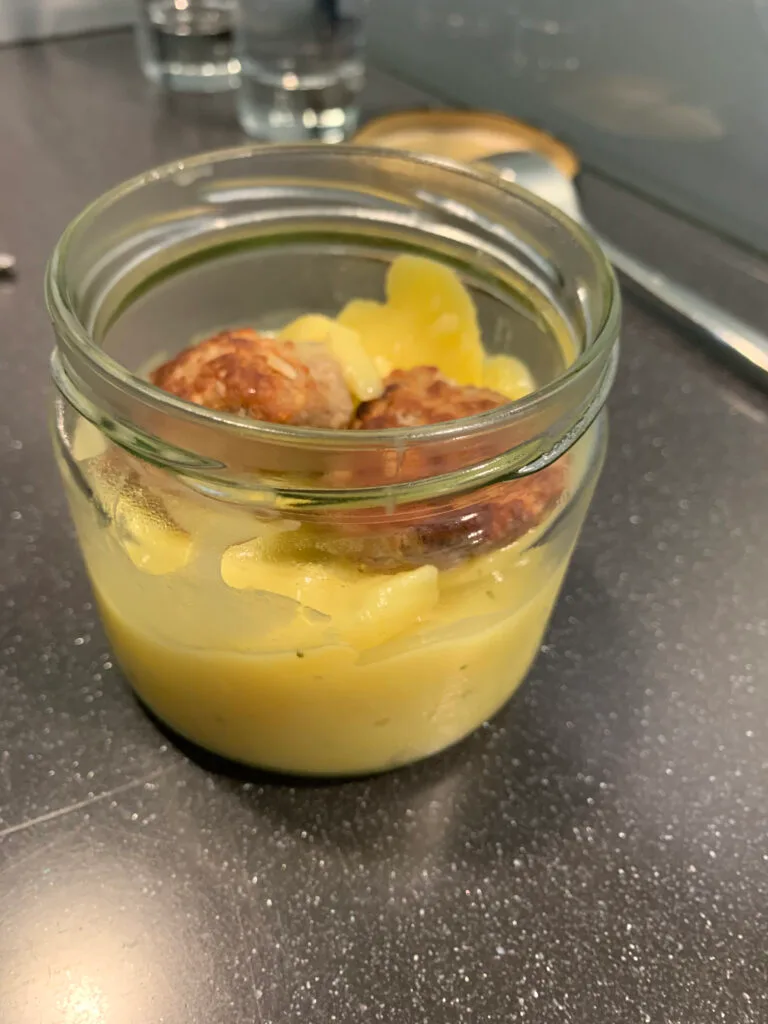 Glasgefäß mit gebratenen Würstchen und gelber Sauce