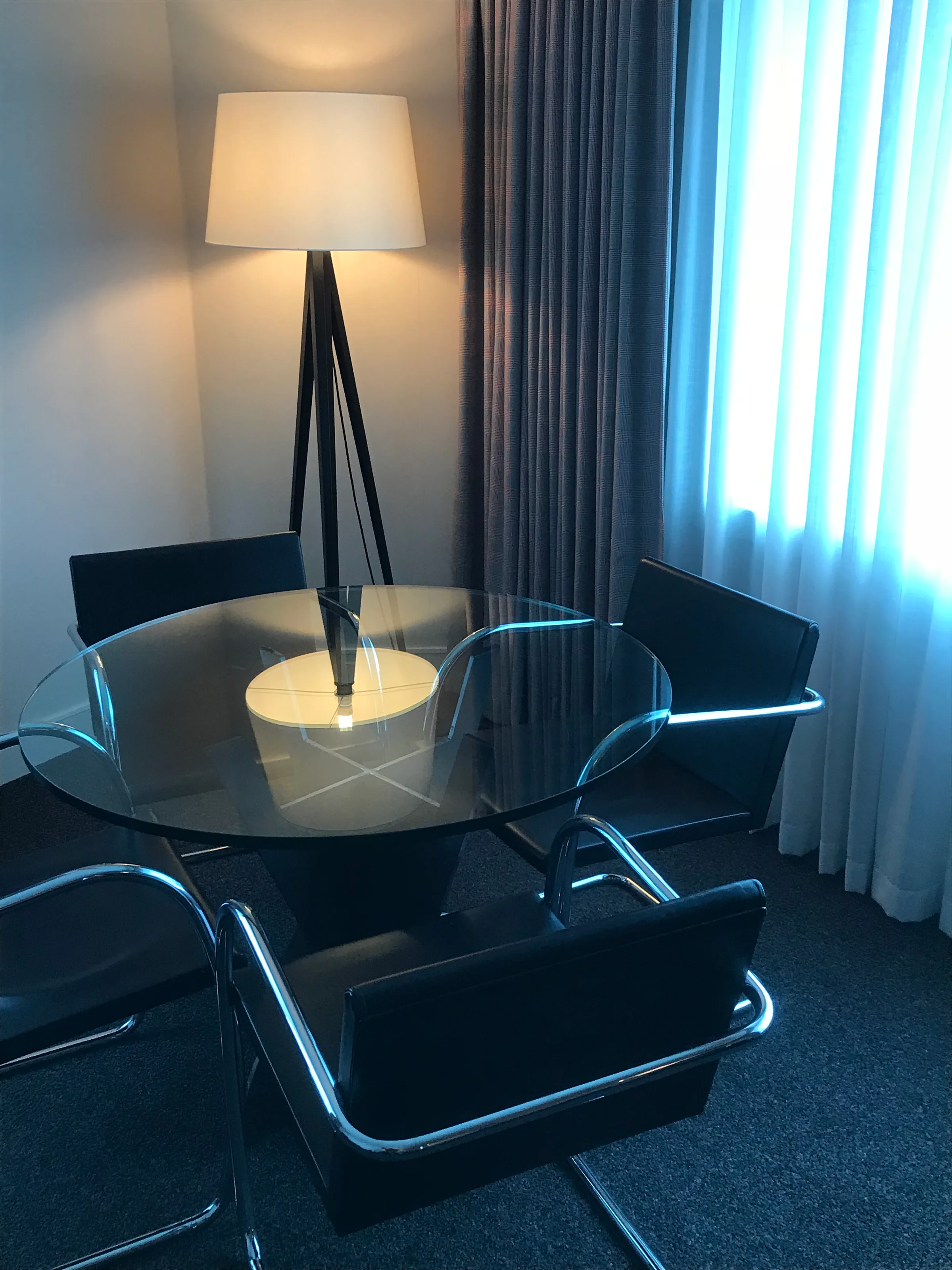 Hotelzimmer mit runder Glas-Tischplatte und schwarzen Stühlen