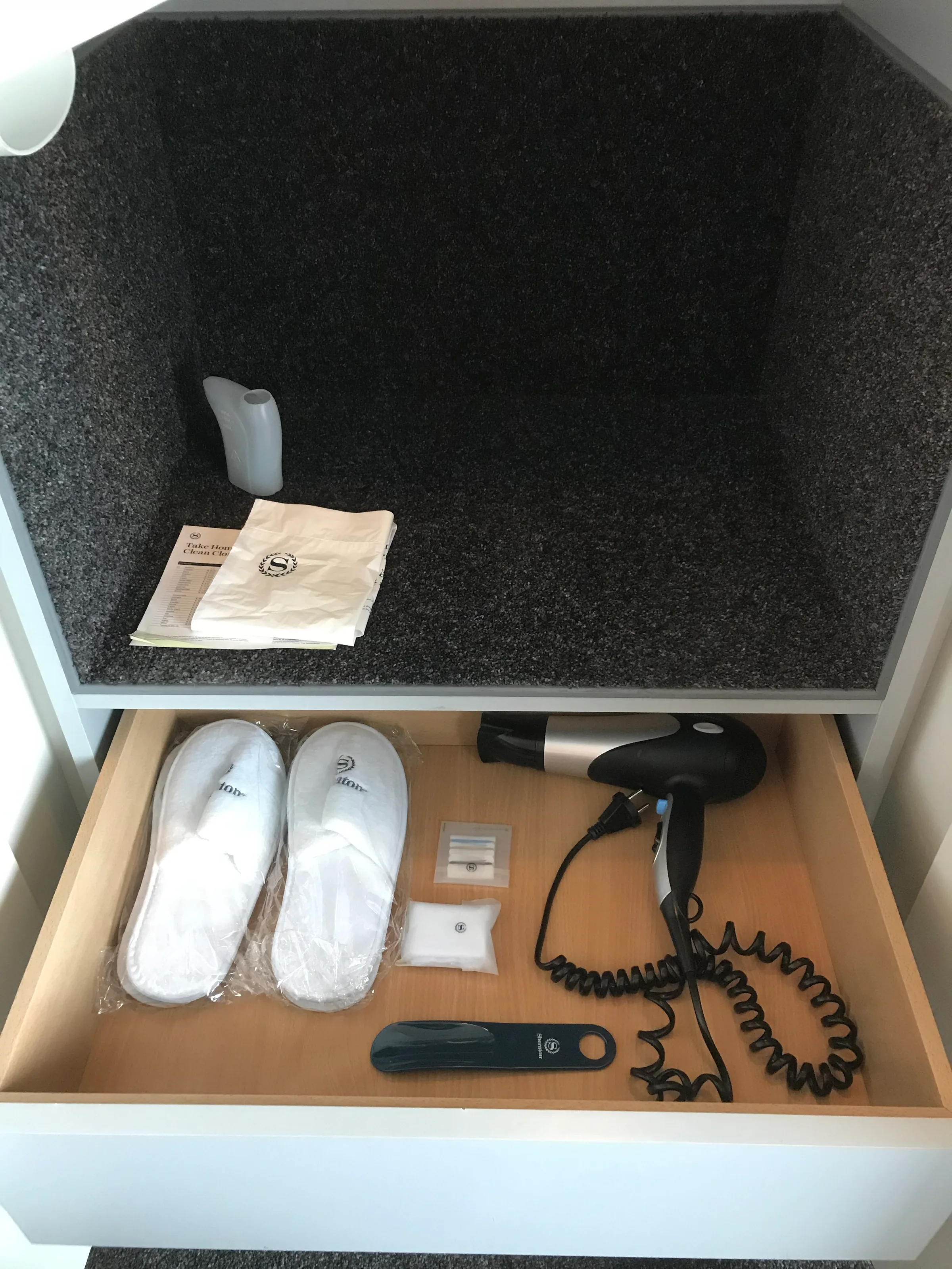 Hotelzimmerschublade mit Haartrockner, Pantoffeln und anderen Gegenständen